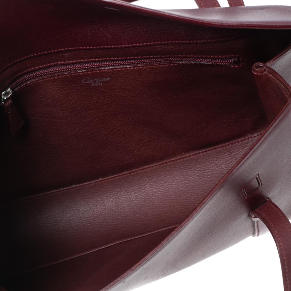 Show your love for Cartier with this Cabochon flap bag from Cartier’s Happy Birthday Collection. This bag is crafted from burgundy leather and features an easy to open flap front, a leather attached silver Cartier logo charm, and short leather