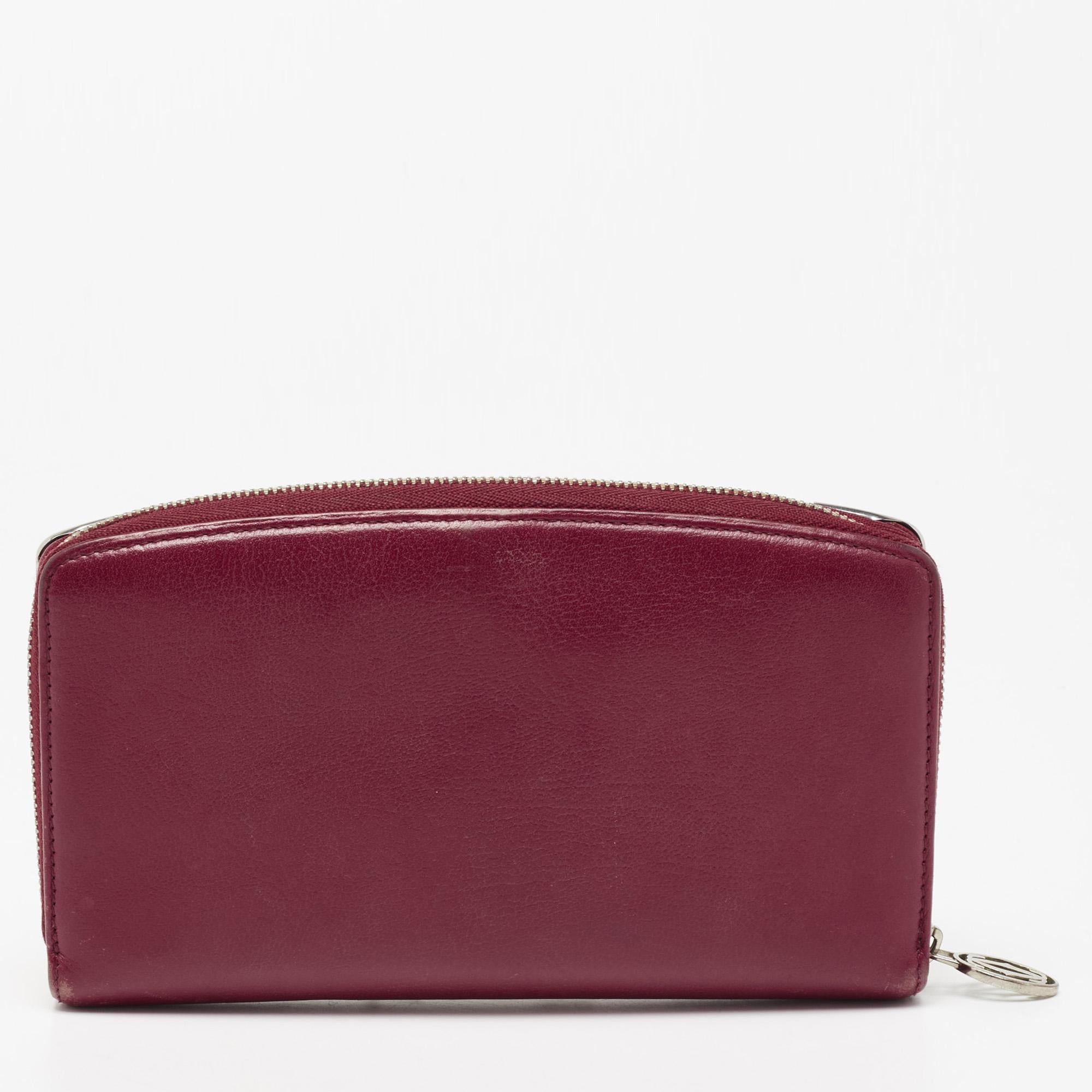 The brand logo on the front makes this Cartier wallet instantly recognizable. It has been made attractive with a burgundy gue and silver-tone accents. Lined with leather and fabric, it has been divided into different compartments and is secured with