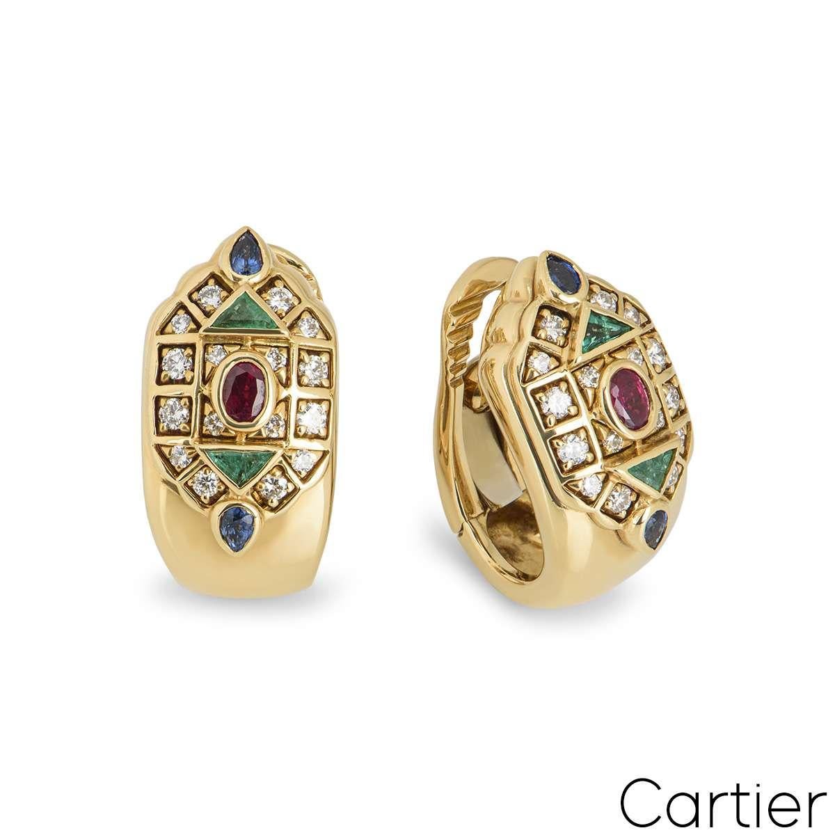A pair of multi stone ear clips from the Cartier Byzantine collection. The front of the ear clip is set with a geometric mosaic of round brilliant cut diamonds, triangular emeralds, pear shape sapphires and oval rubies. Signed Cartier with the