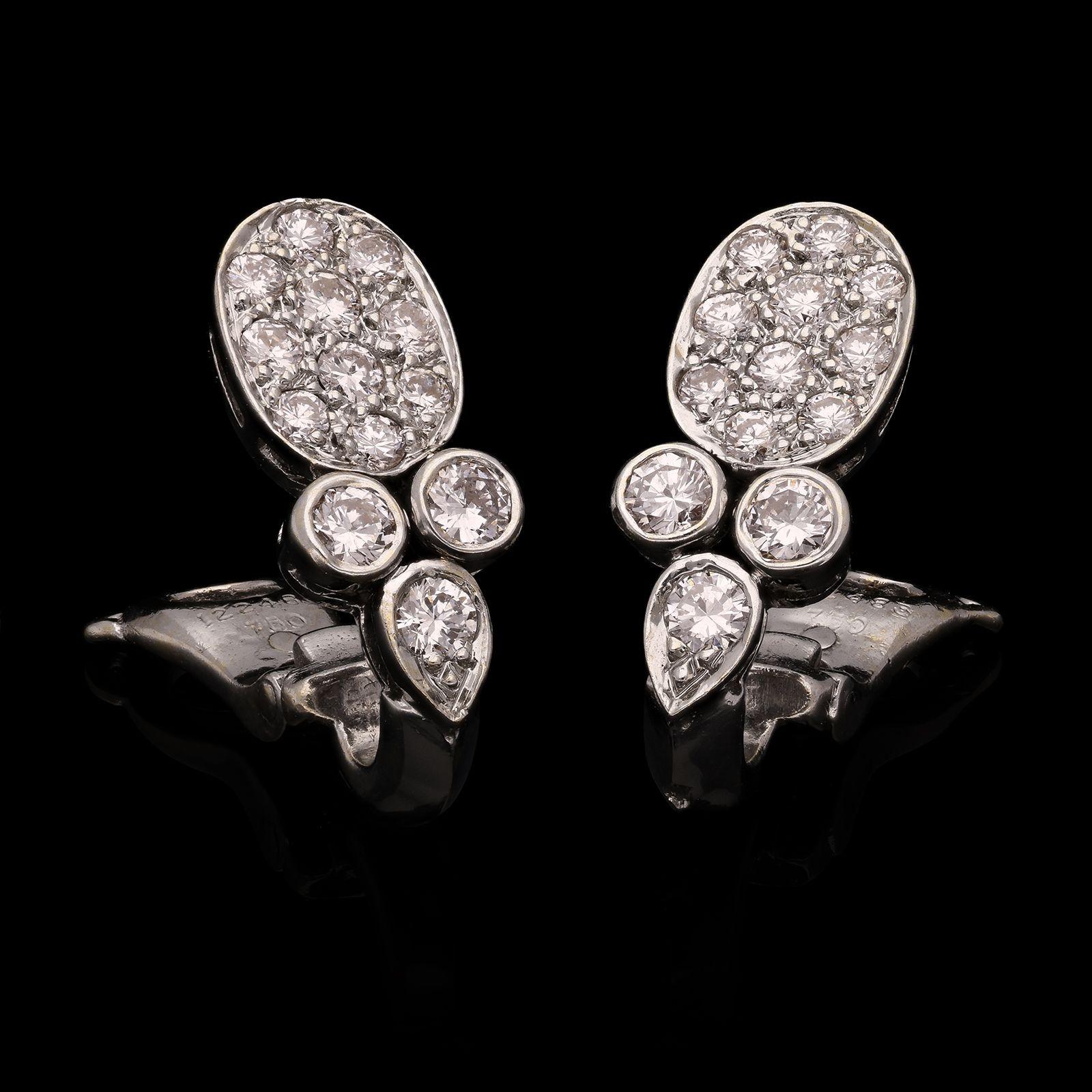 A chic pair of diamond and white gold ear clips by Cartier, each designed as a flat oval motif pavé set with round brilliant cut diamonds above three further round brilliant diamonds, two in bezel settings and one in a pear shape setting, all in