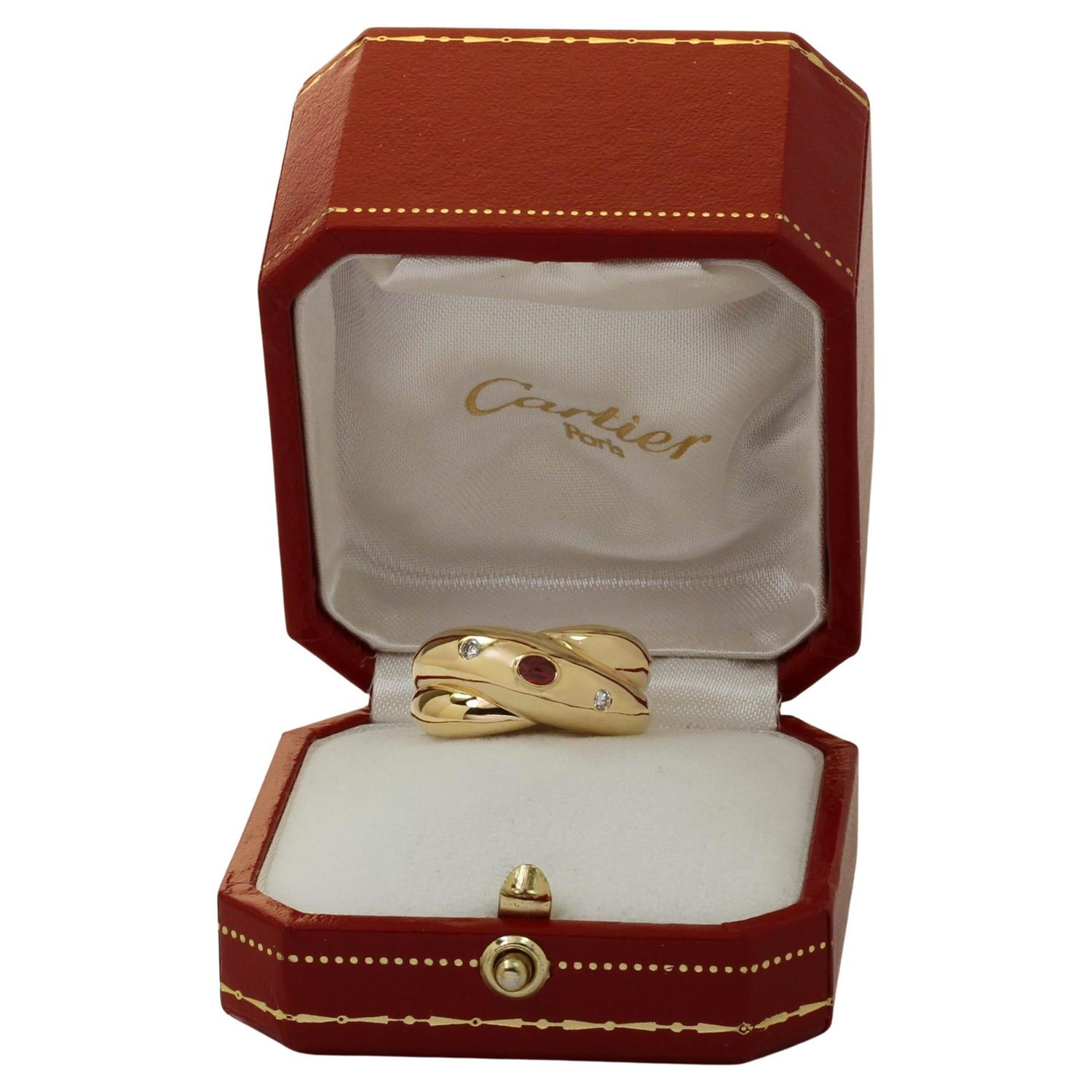 This gorgeous authentic Cartier ring from the elegant Colisee collection features the intertwiend X band motif crafted in 18k yellow gold and bezel-set with a cabochon oval ruby center stone and two round brilliant D-E-F VVS1-VVS2 diamonds. Made in