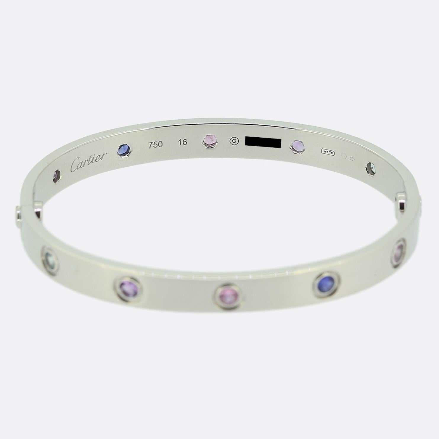 Aquí tenemos un brazalete de oro blanco de 18 ct de la mundialmente conocida casa de joyas de lujo Cartier. Este brazalete forma parte de la colección LOVE y presenta diez piedras preciosas de color junto al icónico motivo del tornillo: espinela