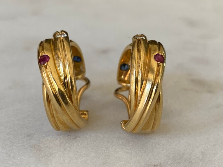 These Estate Cartier lever-back earrings from the classic Constellation collection feature intertwined bands crafted in 18kt yellow gold and set with red rubies, blue sapphires and brilliant-cut round diamonds, F-G color, VS-VVS clarity weighing