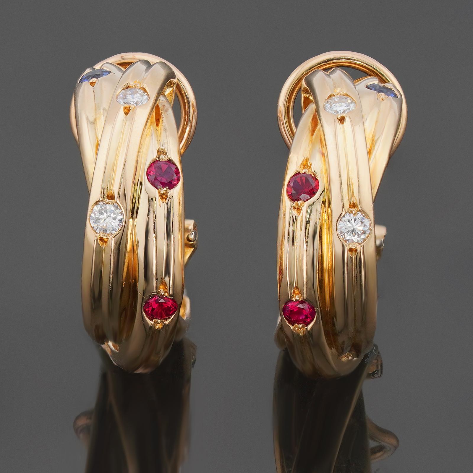 Estos magníficos pendientes envolventes Cartier de la clásica colección Constelación presentan bandas entrelazadas elaboradas en oro amarillo de 18 quilates y engastadas con rubíes rojos, zafiros azules y diamantes redondos talla brillante D-E-F
