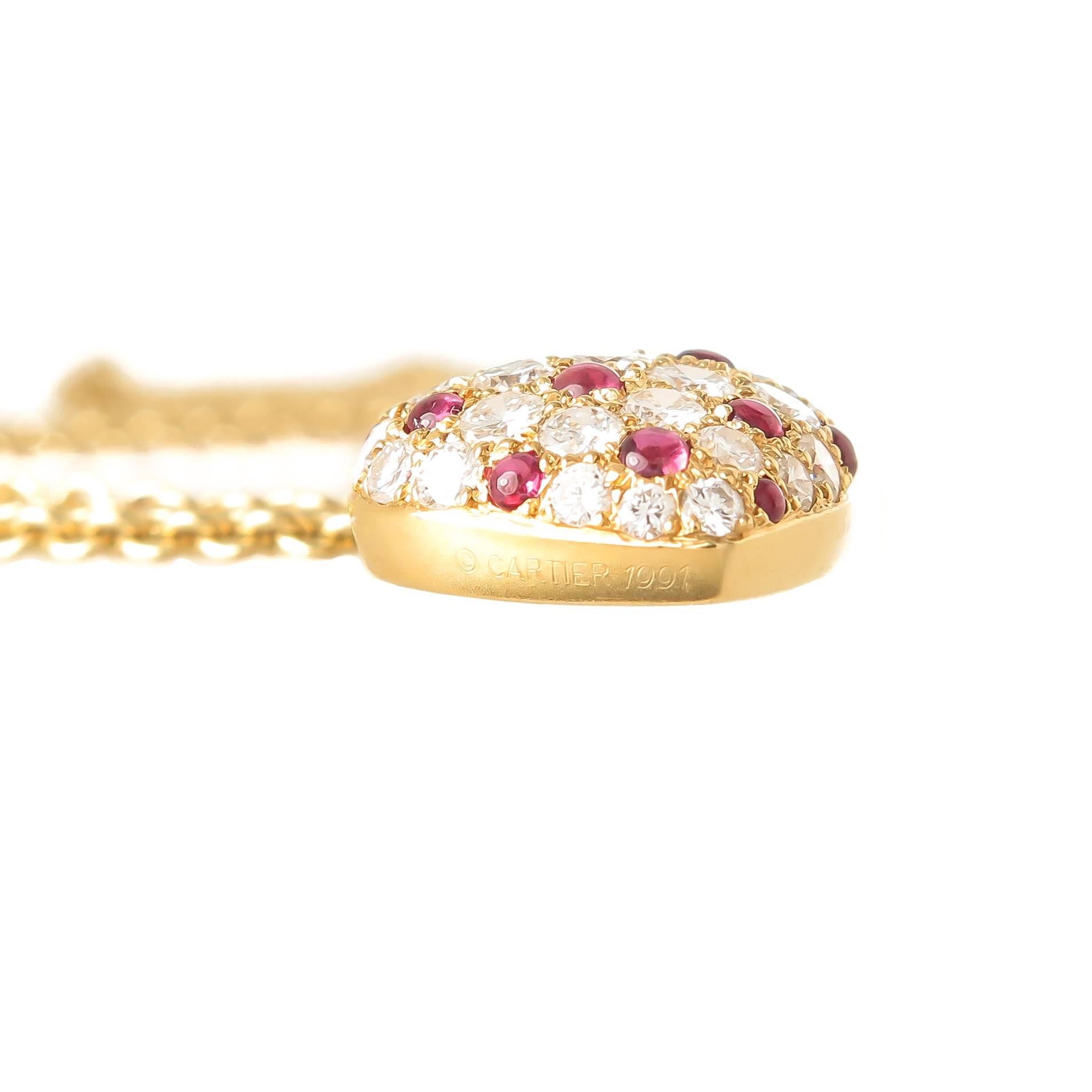 Circa 1990s Cartier 18K yellow Gold Heart Pendant Necklace, measuring 7/8 X 5/8 inch and set with Round Brilliant cut Diamonds totaling 1.50 Carats and Grading as F-G in color and VS in clarity, further set Cabochon Rubies of Very Fine Color and