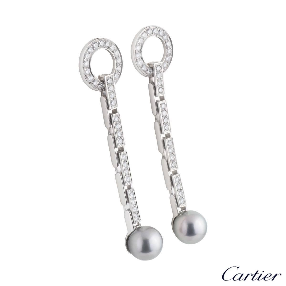 A beautiful pair of 18k white gold Cartier diamond and pearl drop earrings from the Agrafe collection. The earrings each comprise of a open work circular motif pave set with round brilliant cut diamonds. Complementing this motif is a flexible