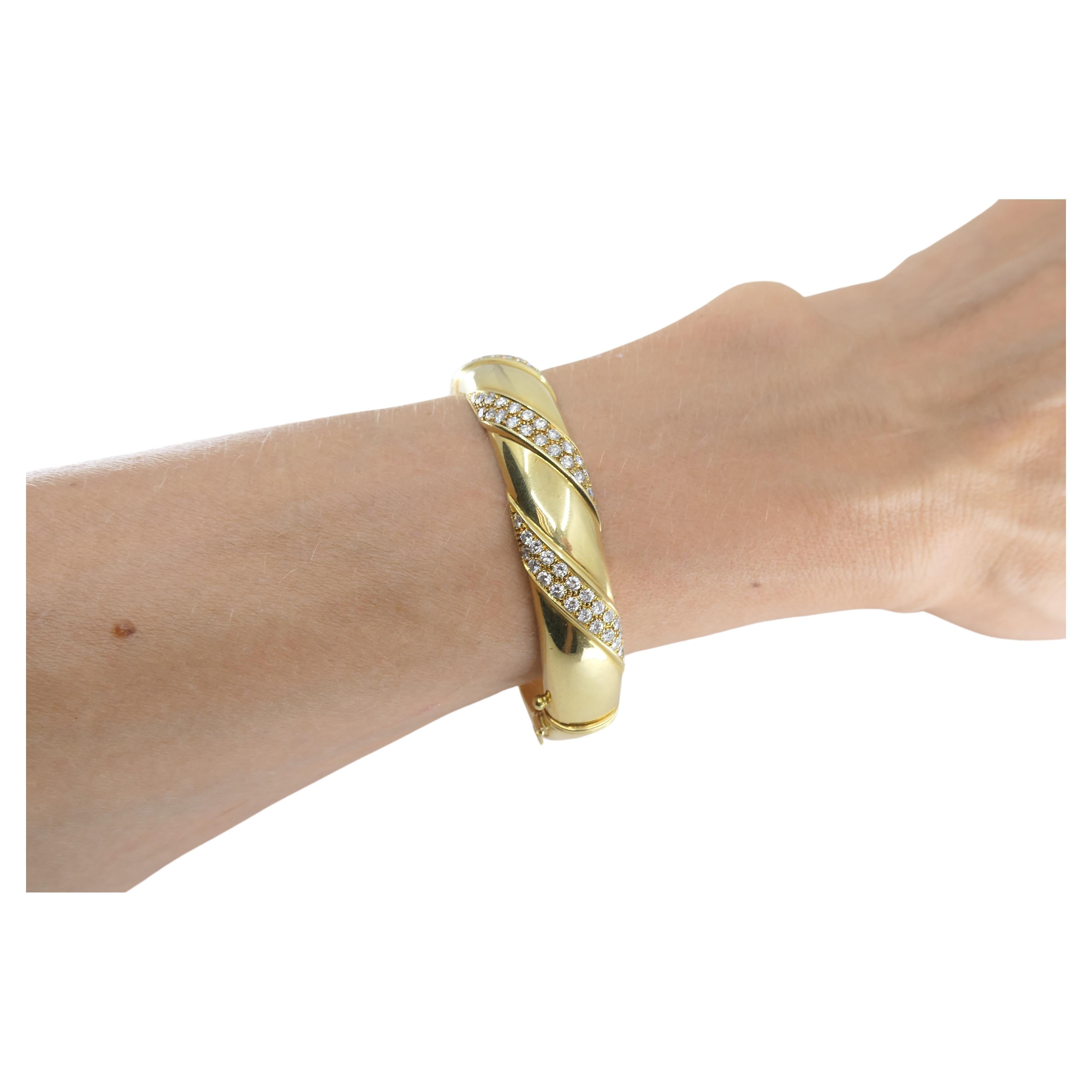 An elegant Cartier diamond bracelet, crafted from 18k gold, circa 1970s. This polished gold bangle features three rows of diamonds arranged in a double-ribbon design that wraps gracefully around the bracelet. This Cartier diamond bracelet is silky