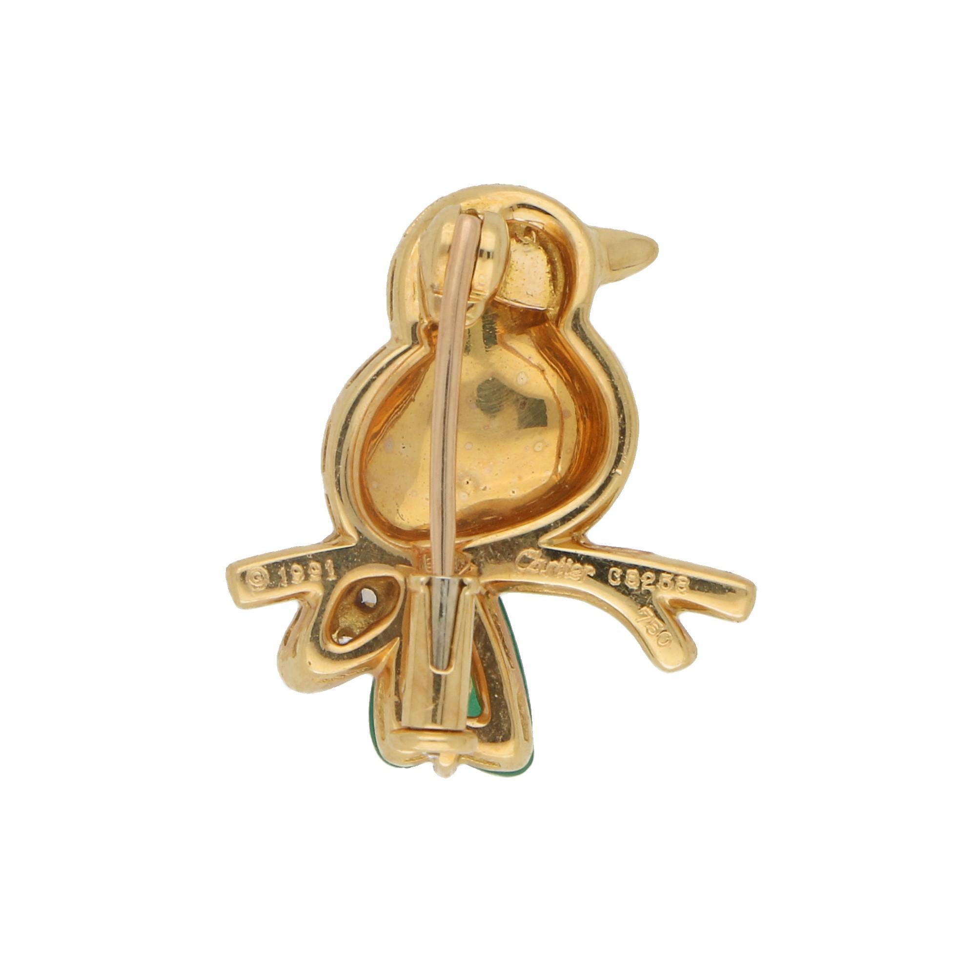 An adorable little Cartier bird pin/brooch set in 18k polished yellow gold. The pin depicts a sweet little bird perched on an onyx set branch. Its wing is set with exactly 12 round brilliant cut diamonds and a singular piece of carved chalcedony to