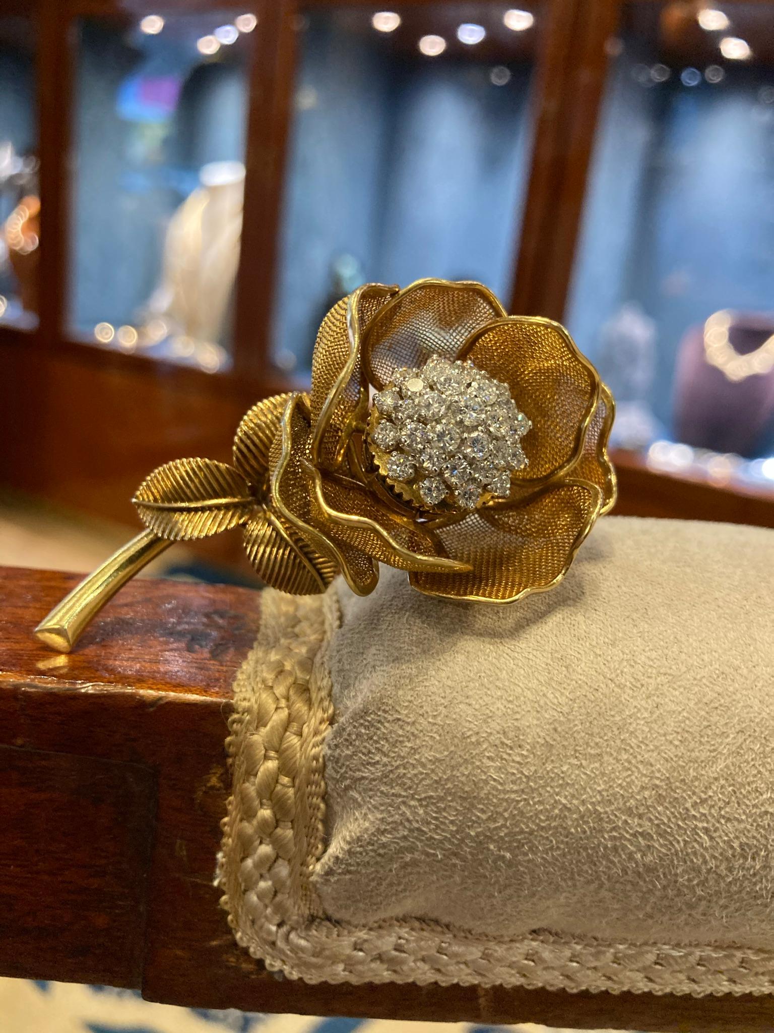 A beautiful Cartier flower brooch in 18 karat yellow gold with gold mesh petals surrounding a center cluster of round brilliant cut diamonds, and three fluted leaves. France, circa 1950s. The petals can be opened and closed.