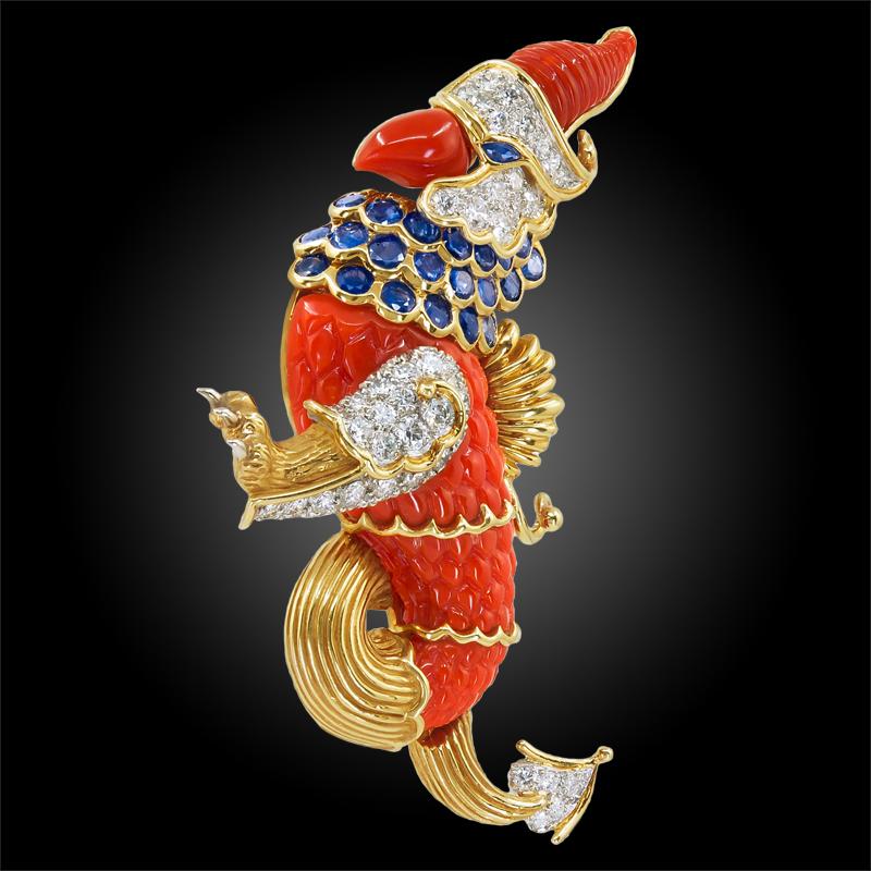 An 18k gold brooch, designed as a griffin, composed of carved coral and set with round sapphires and diamonds, the leg, tail, and wing of textured gold, signed Cartier, 1960s.
dimensions approx. 3″ x 1 1/2″
