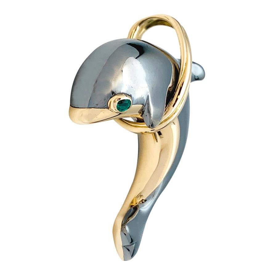 A 18Kt yellow gold and Silverium dolphin Cartier pendant, jumping through a three colors of gold hoop. The eye is represented by an oval emerald, 
SILVERIUM is a silver-based alloy and is a trademark by Cartier International B.V.
The registration