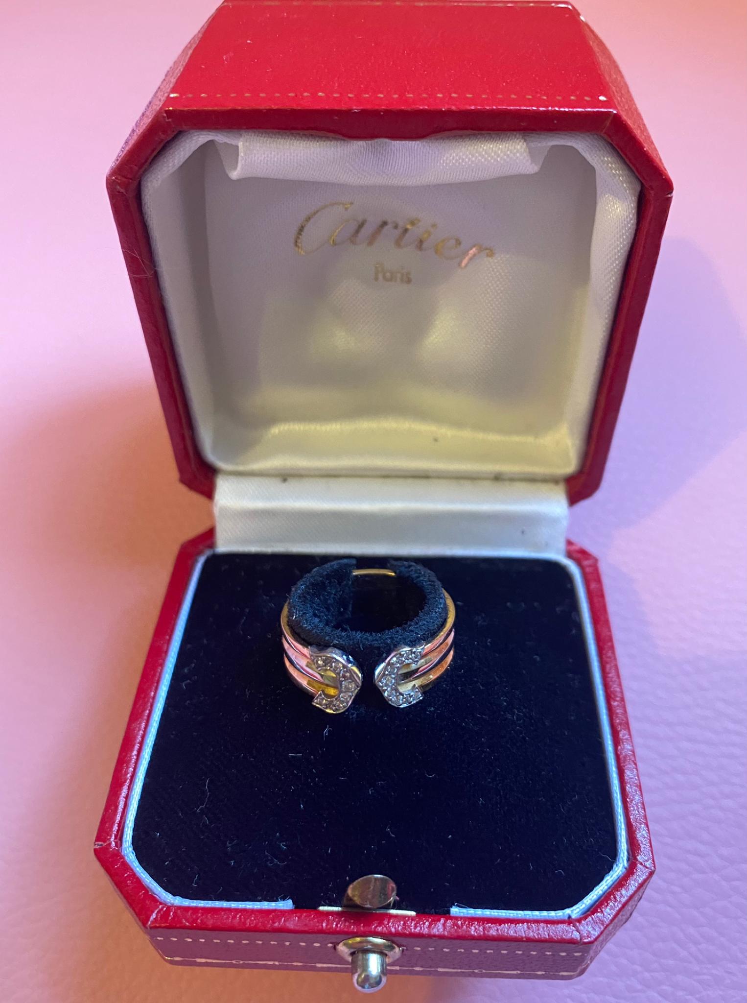 Este elegante anillo abierto Cartier presenta un diseño de tres tonos, elaborado en amarillo de 18 quilates, blanco de 18 quilates y completado con los icónicos extremos en forma de Doble C engastados con diamantes redondos talla brillante. El