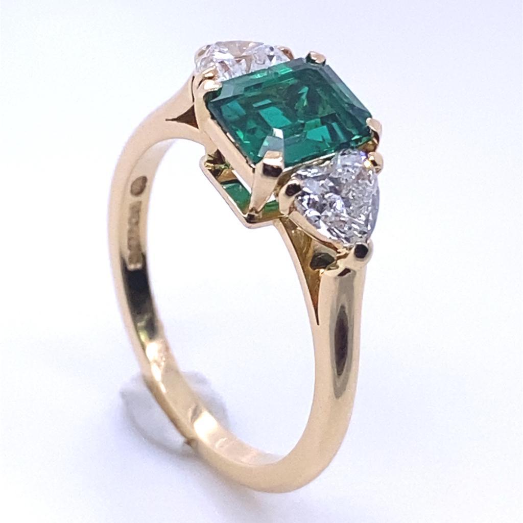 A Cartier emerald and diamond three stone 18 karat yellow gold ring, circa 1997.

This exceptional ring by Cartier is set to its centre with an emerald cut emerald of 1.03 carats and framed by a heart shaped diamond either side for a total of 0.90