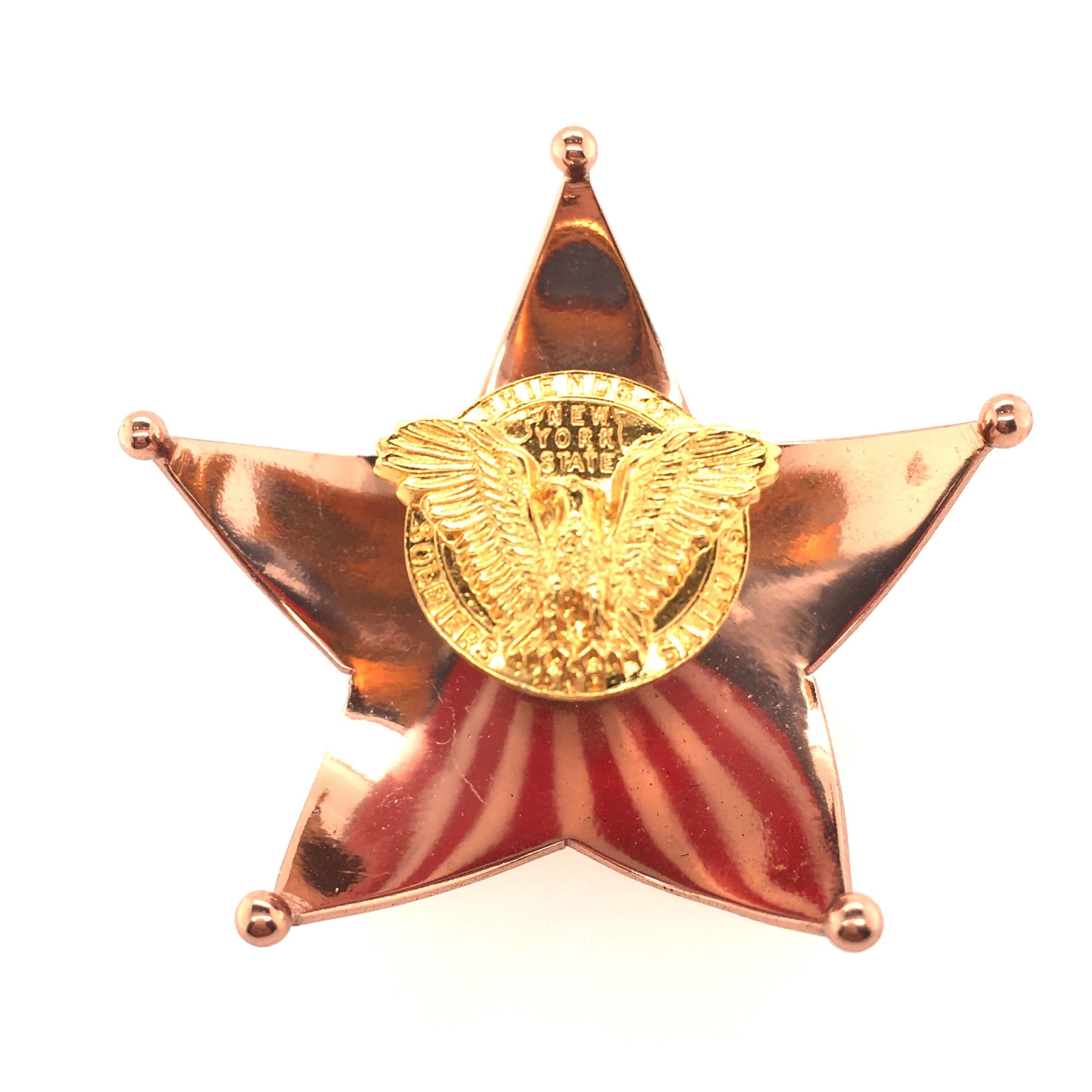 A gilt metal and enamel Stars and Stripes brooch, Cartier, circa 1940. Designed as a copper colored curving star, centering a flared en tremblant segment applied with red, white and blue enamel in an American flag motif, surmounted by an emblem of