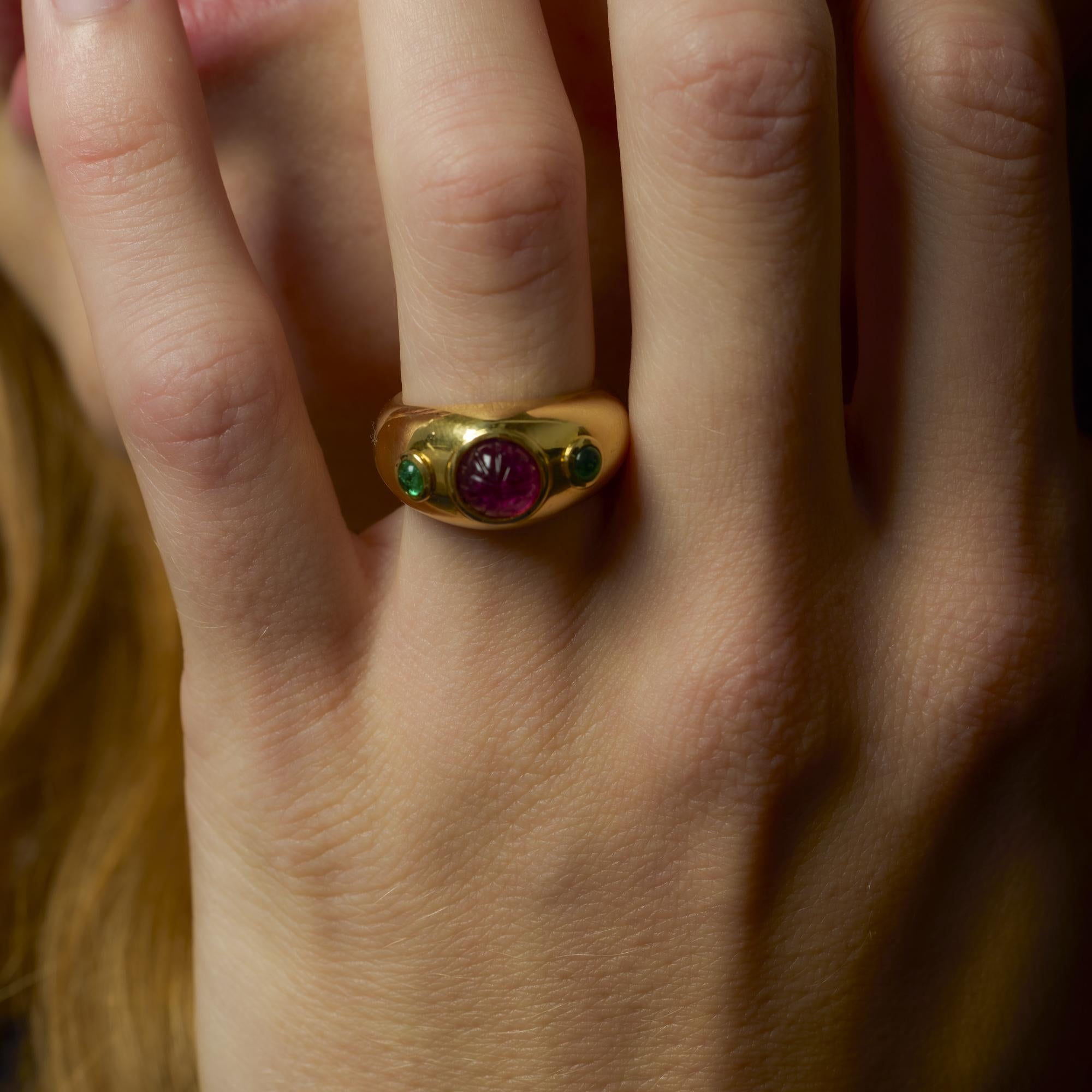 Dieser kühne Ring von Cartier zeigt einen reich geschliffenen rosafarbenen Saphir, der von Cabochon-Smaragden umrahmt wird, in einer markanten Fassung aus 18 Karat Gelbgold, signiert und punziert.