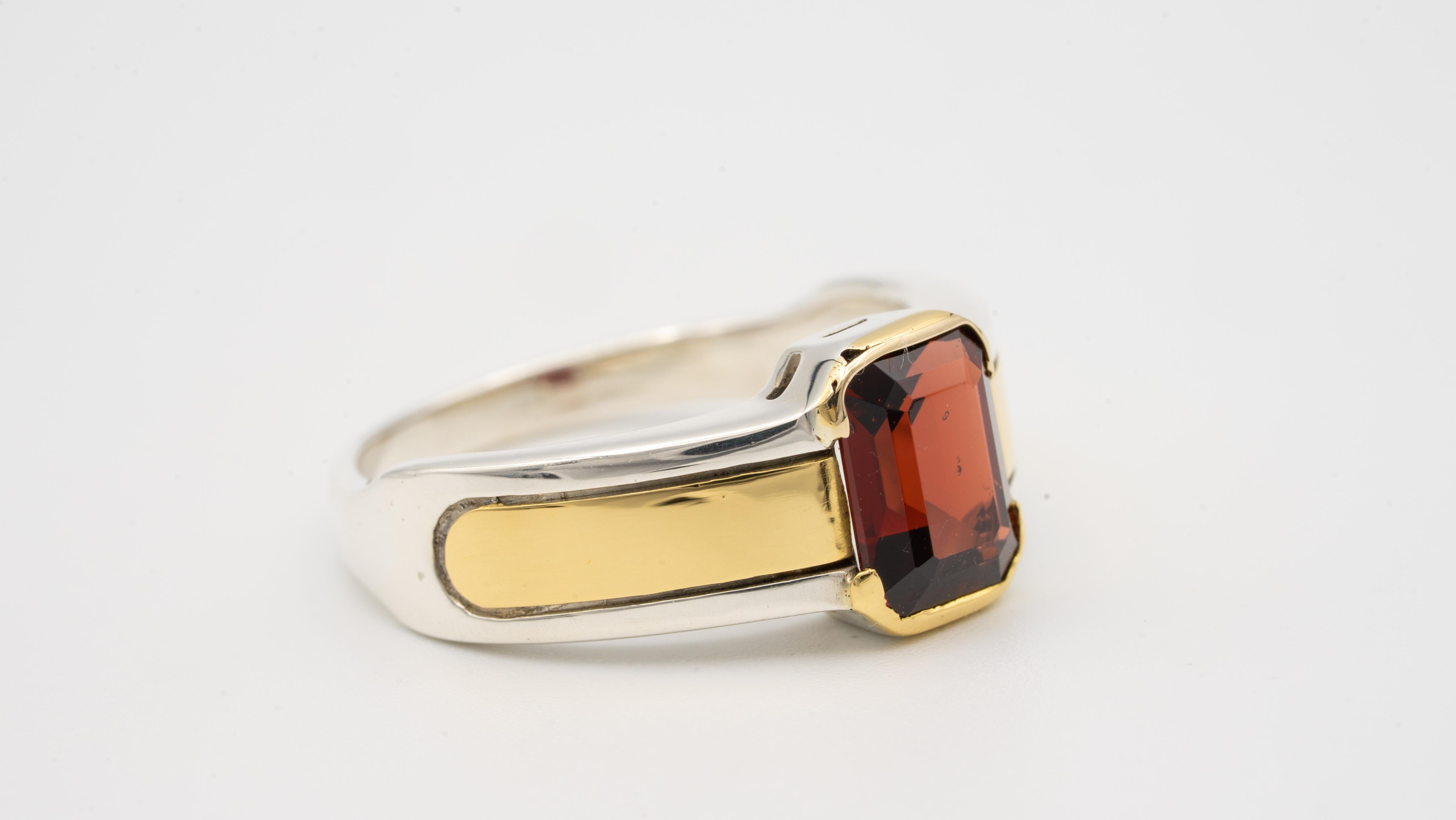 Cartier Ring finely crafted in Sterling Silver and 18 Karat yellow gold featuring an emerald cut Garnet in the center.
Garnet weighs 1.50 carats approximately. Garnet has a red lively color and is set in a thin half bezel.
Measurements: 5.78 mm at
