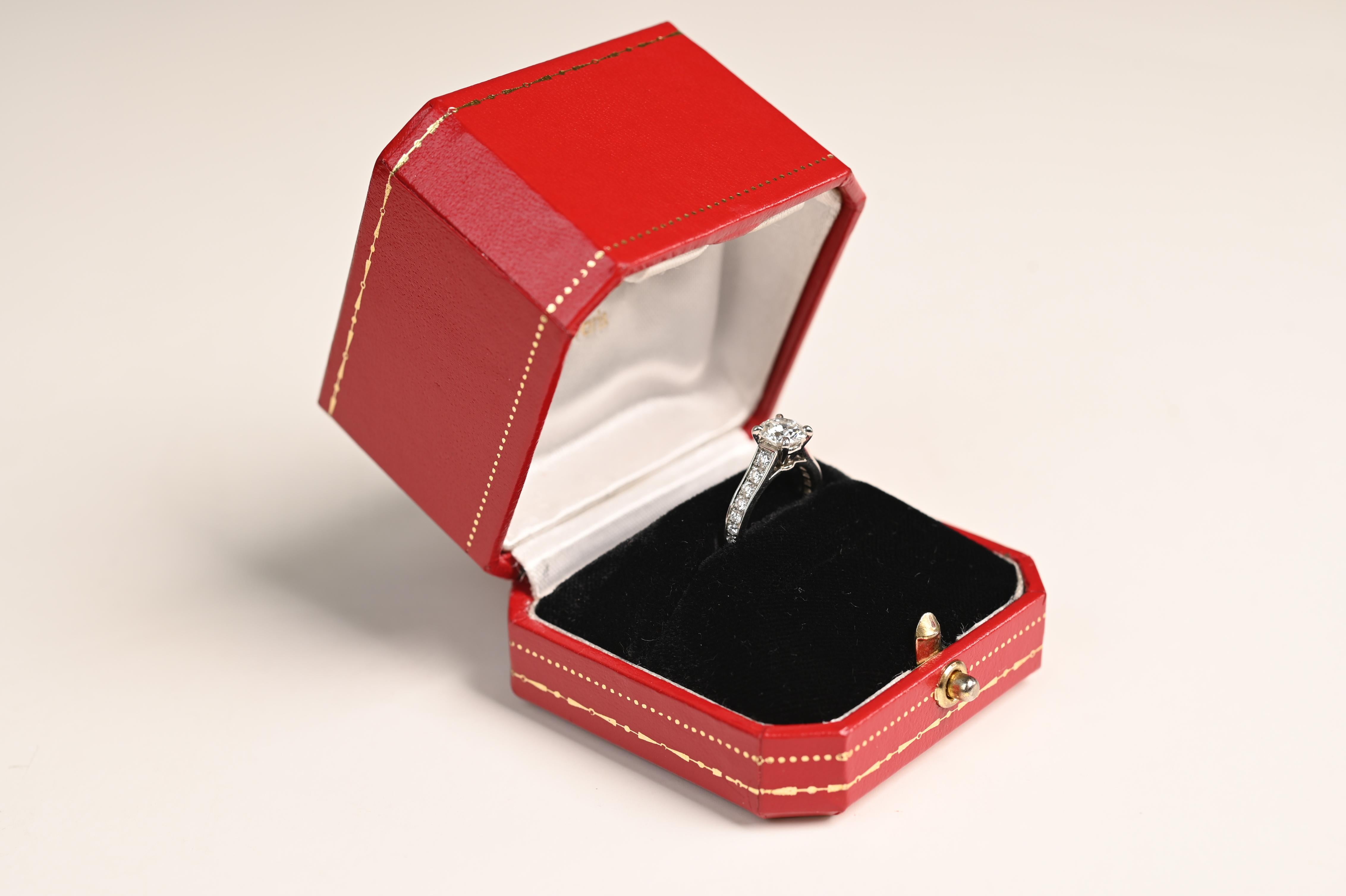 Nous vous présentons une bague de fiançailles Cartier à couper le souffle, un exemple exquis d'élégance intemporelle et de savoir-faire magistral. En son centre se trouve un éblouissant diamant rond de taille brillant pesant environ 1 carat. Cette