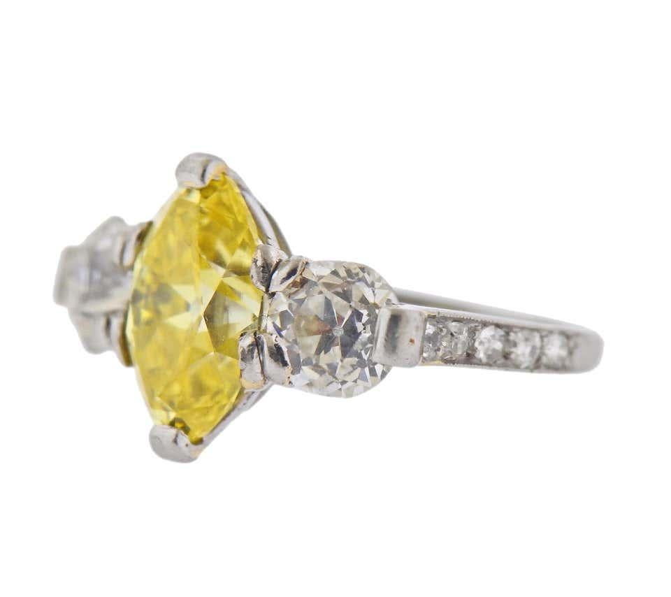 Cartier platinum engagement ring, set with a center GIA certified 3.15ct Fancy Vivid Yellow/VVS2 marquise cut diamond, with two approx. 0.70ct old mine cut diamonds on sides, and small diamonds in the setting. Ring size - 4.5. Marked: Cartier.