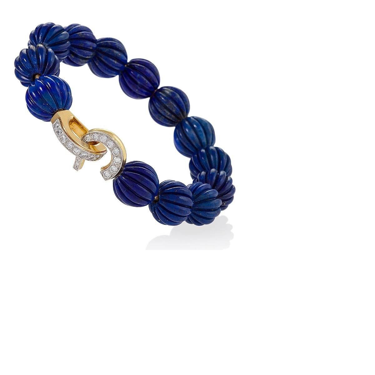 A French mid-20th century 18 karat gold bangle with lapis lazuli and diamonds by Cartier, Paris. The bracelet is  composed of 13 melon-carved lapis beads completed by a scroll and arch design platinum-topped 18 karat gold and clasp, highlighted by