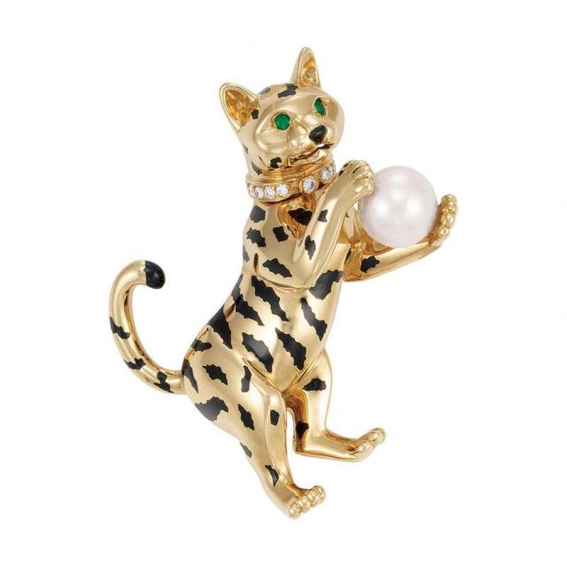 The playful cat grasping one cultured pearl approximately 9.4 mm., its body applied with black enamel stripes, accented by 2 small round emerald eyes, decorated with a diamond-set collar, signed Cartier, #652818, with maker's mark and French assay