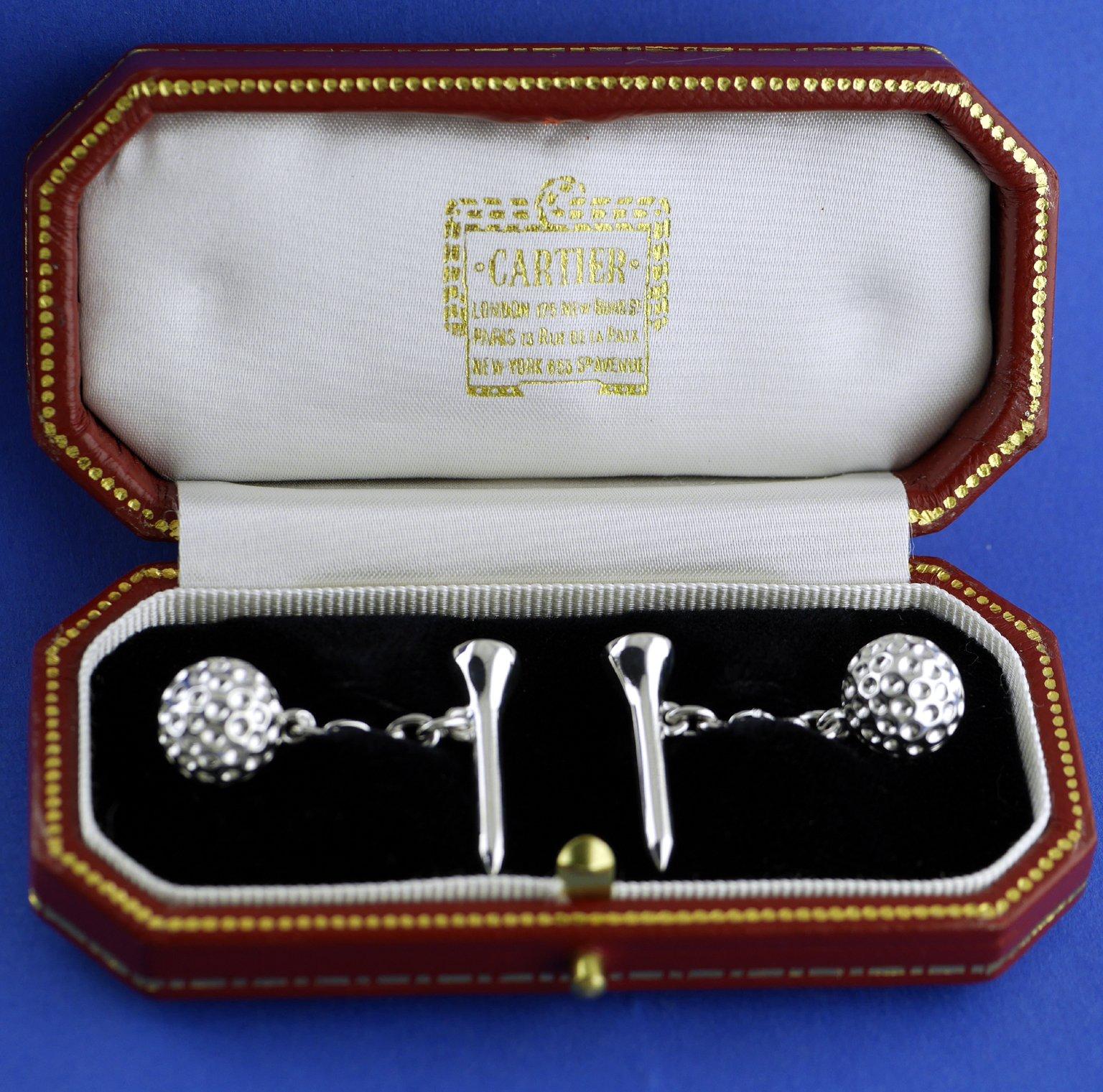 A pair of 18 carat white gold cufflinks by Cartier depicting a golf ball and tee circa 1970.

In fitted Cartier Box.

Dimensions:

Overall Length (including Ball, Chain and Tee) 29mm

Golf Ball (Diameter) 10mm 
Tee (Height) 22mm
Tee (at widest