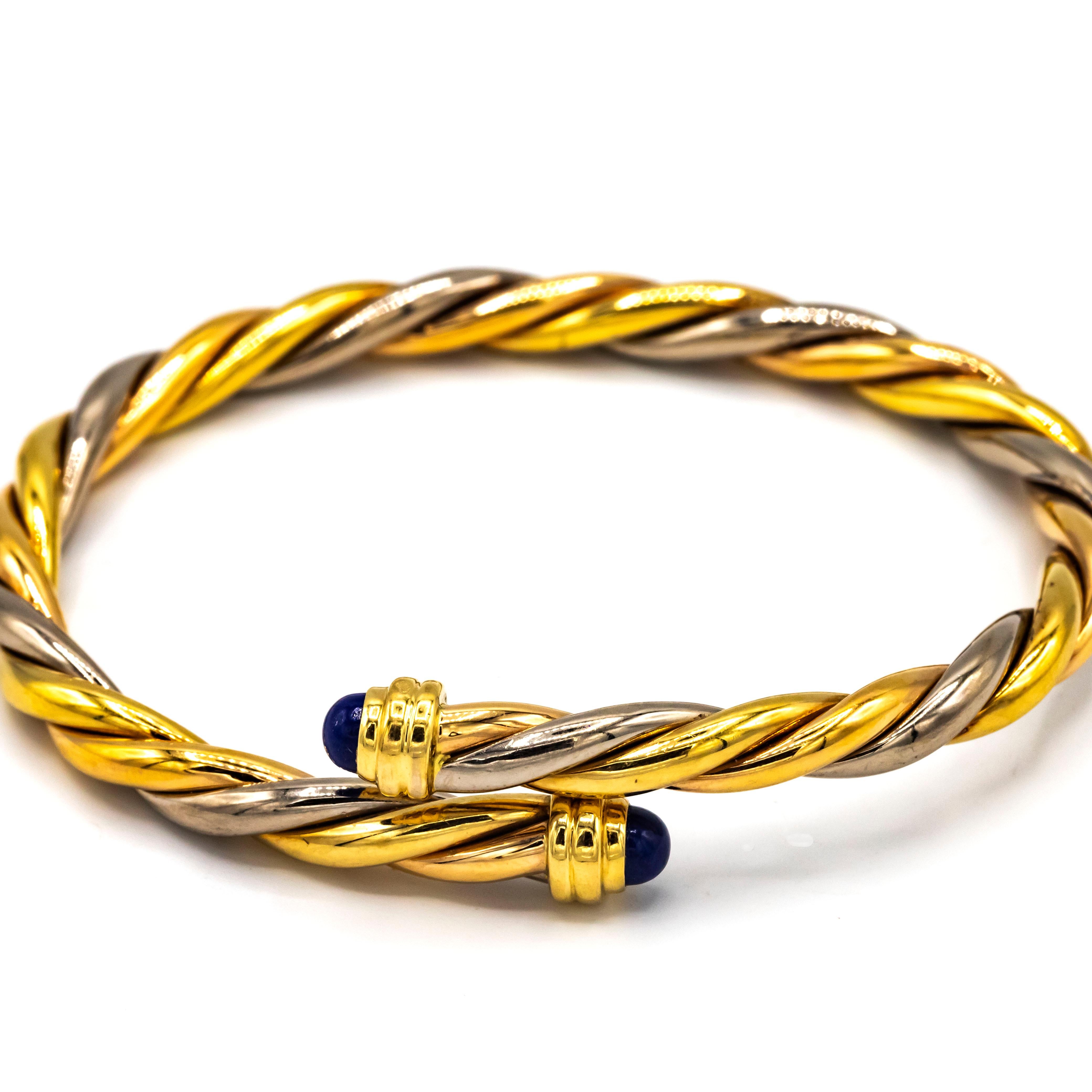 Cartier tricolor 18K gold lapis lazuli twisted bypass cuff bangle bracelet featuring two round cabochon lapis lazuli gemstone end caps. The total net weight is approximately 25 g. (The Cartier box and papers are not included.) 

Measurements: Inside