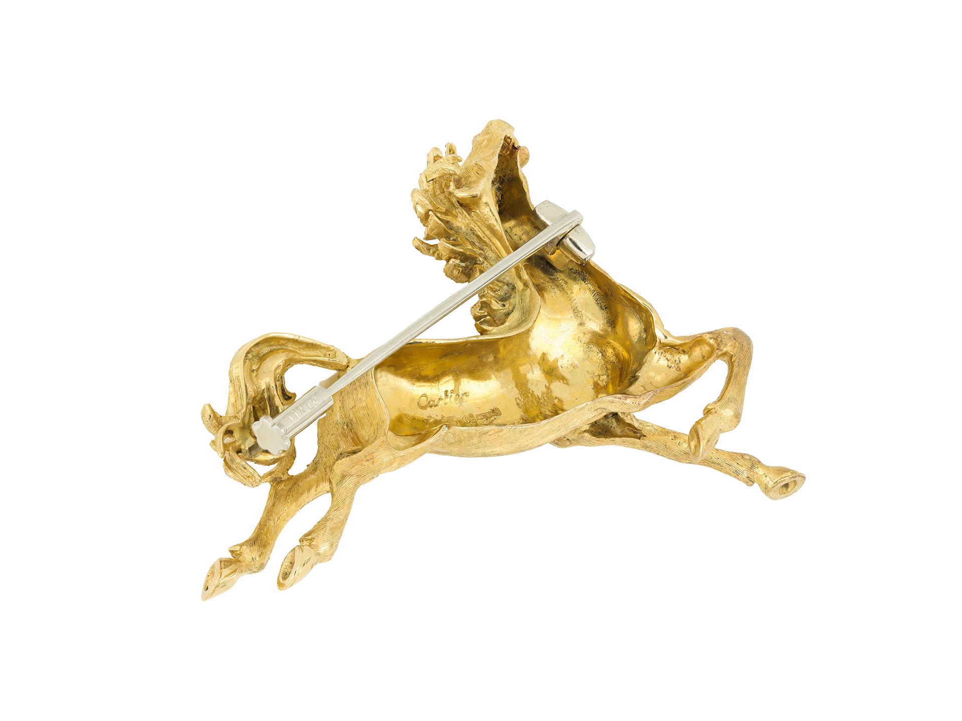 Cartier horse brooch. A yellow gold brooch in the form of a horse, set with one round cabochon natural ruby in an open back rubover setting with an approximate weight of 0.03 carats, to a dynamic horse brooch featuring intricate carving and textured