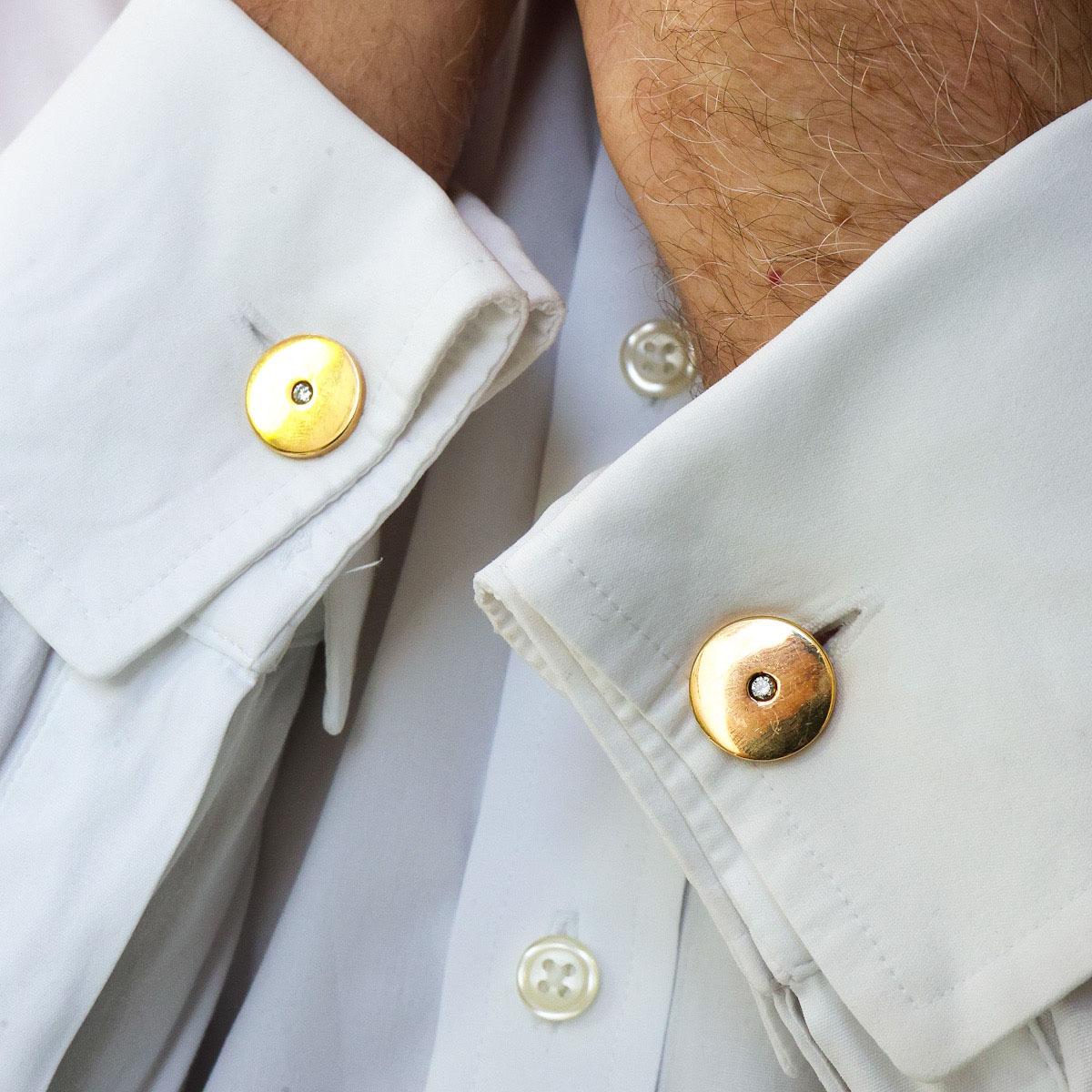 A pair of Cartier diamond and gold disc cufflinks, with a round brilliant-cut diamond in the centre of each polished disc, with flat curved fixed bar links, hinged at one end, onto smaller gold discs, signed Cartier, in script and capitals, dated