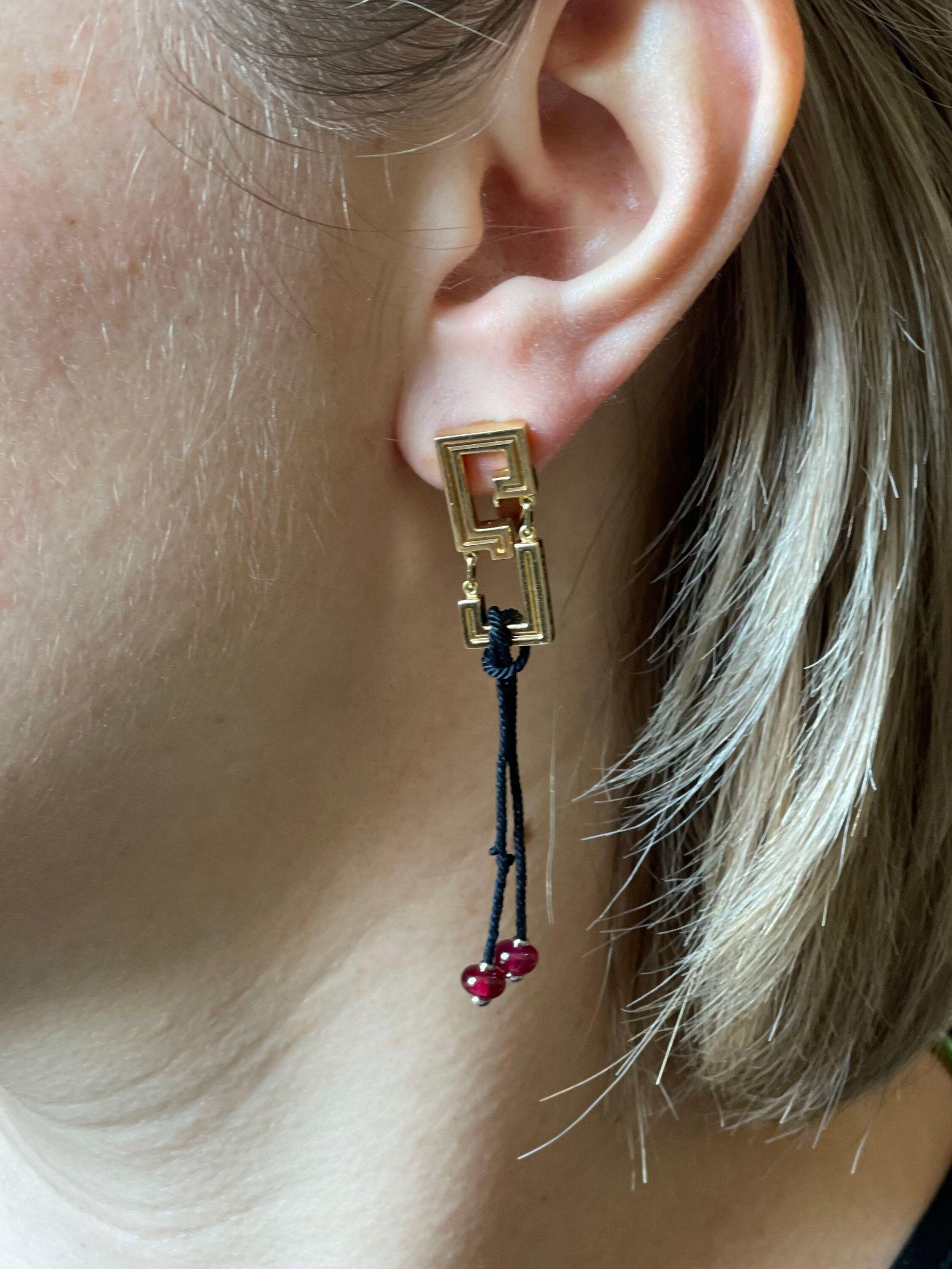 Pair of 18k gold earrings by Cartier, from La Baiser du Dragon collection, featuring black cord drops with ruby cabochons. Earrings are 2.5