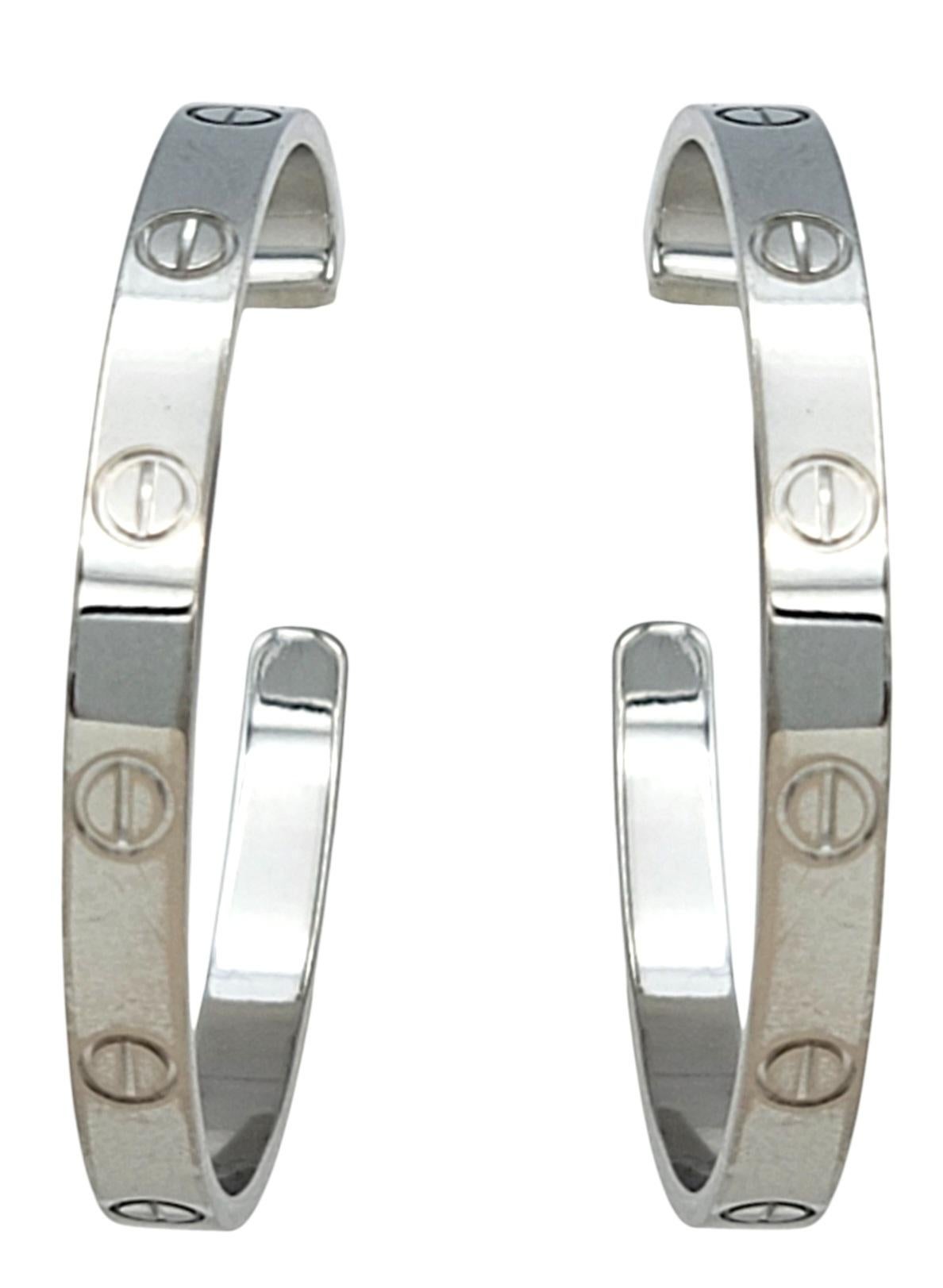 Aggiungi un'eleganza senza tempo alla tua collezione con questi autentici orecchini a cerchio Cartier Love, realizzati in lussuoso oro bianco 18 carati. Questi orecchini dell'iconica collezione Love sono impreziositi dal caratteristico motivo a