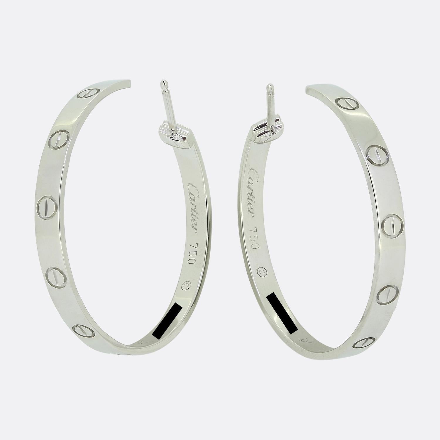Aquí tenemos un maravilloso par de pendientes con aro de la mundialmente conocida casa de joyas de lujo Cartier. En conjunto, estas piezas idénticas forman parte de la colección LOVE y han sido elaboradas en oro blanco de 18 quilates con el borde