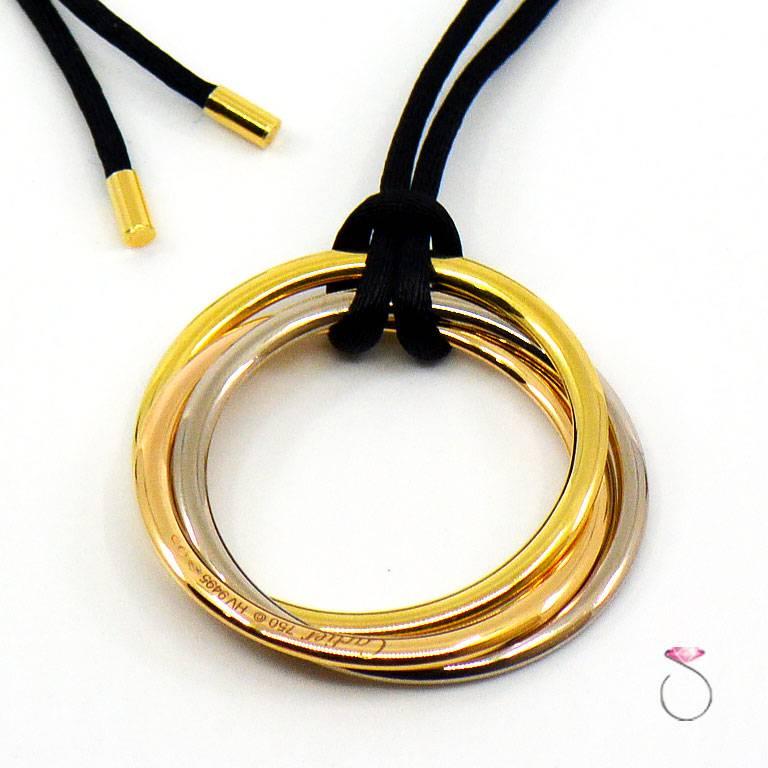 Stunning Cartier Large Trinity Necklace in 18k yellow, white & rose gold on black cord with gold ends & slider. This iconic Cartier necklace features a pendant of three large tricolor interlaced rings, in yellow, white and rose gold on a black cord.