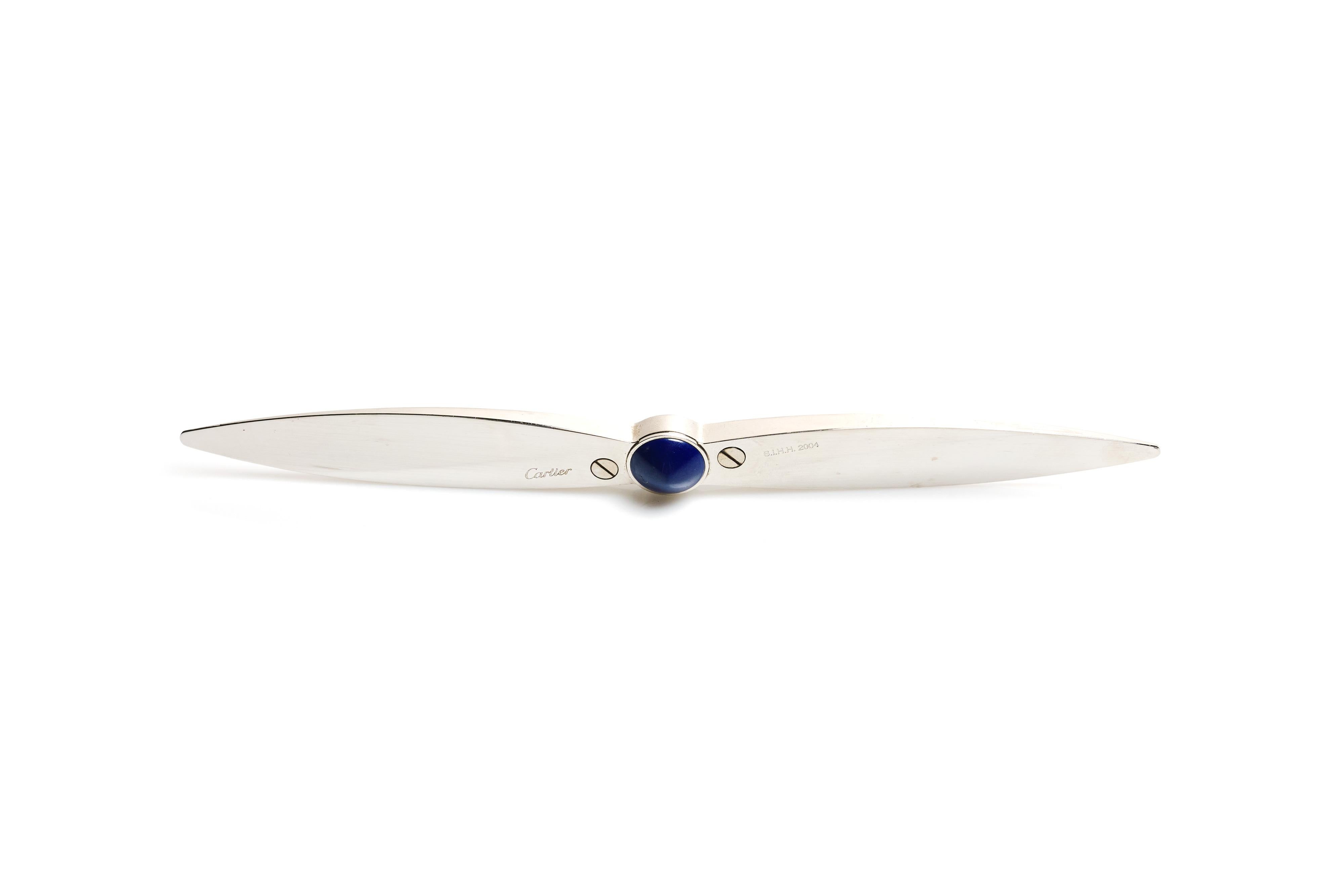 A beautiful letter opener by Cartier, done in silvered brass with a lapis cabochon set into the center. Crafted in the form of an airplane propeller.

Marked on edge near center.