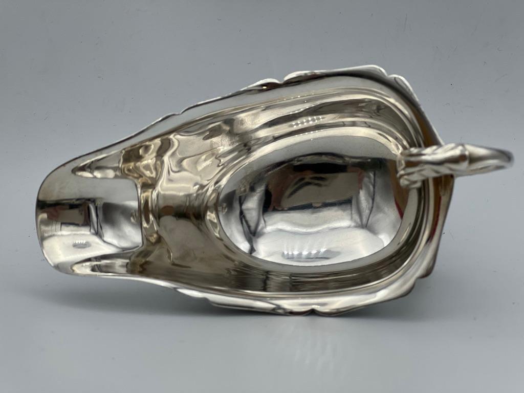 Cartier London sterling silver sauce boat with footed base. Scalloped border with scalloped handle, engraved work at top. Hand crafted in the Cartier London workshop. Beautiful, functional, and timeless design by Cartier.