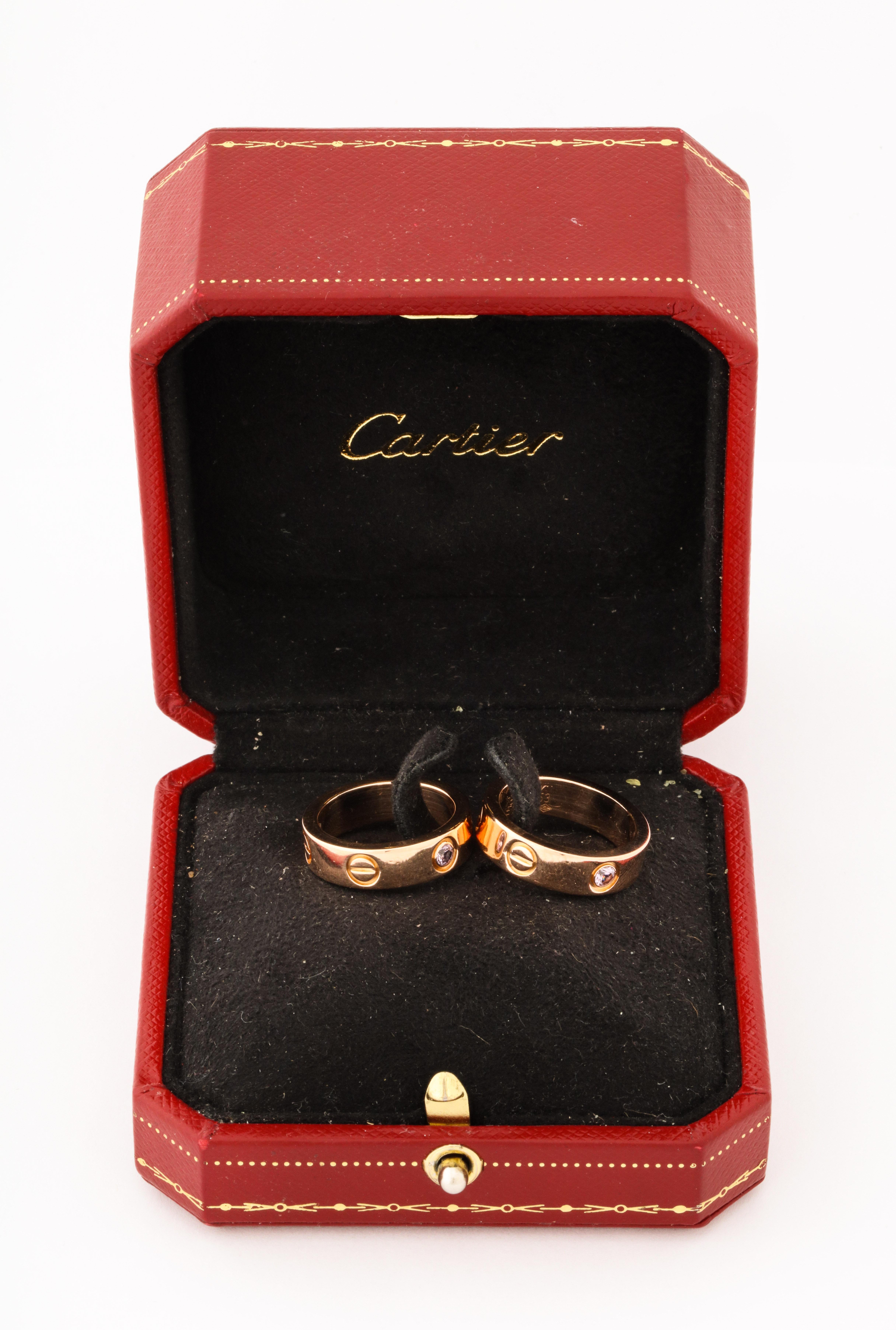 A pair of Cartier 18K Love rings with pink sapphires. They are a matching pair worn 
together with one a little larger to accommodate the fit.
They are in the original Cartier box. 
