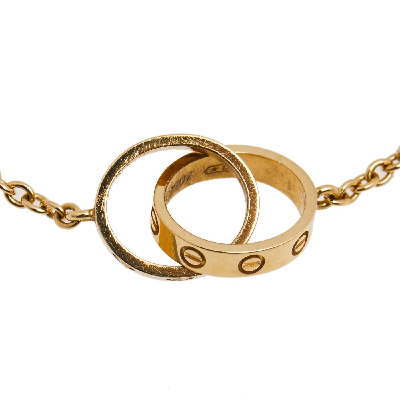 Celebrate timeless love with this bracelet from Cartier's Love collection. Made from 18k yellow gold, it has a chain that holds two magnificent rings interlocked with one another. On both, one can see the iconic screw motifs which are a signature of