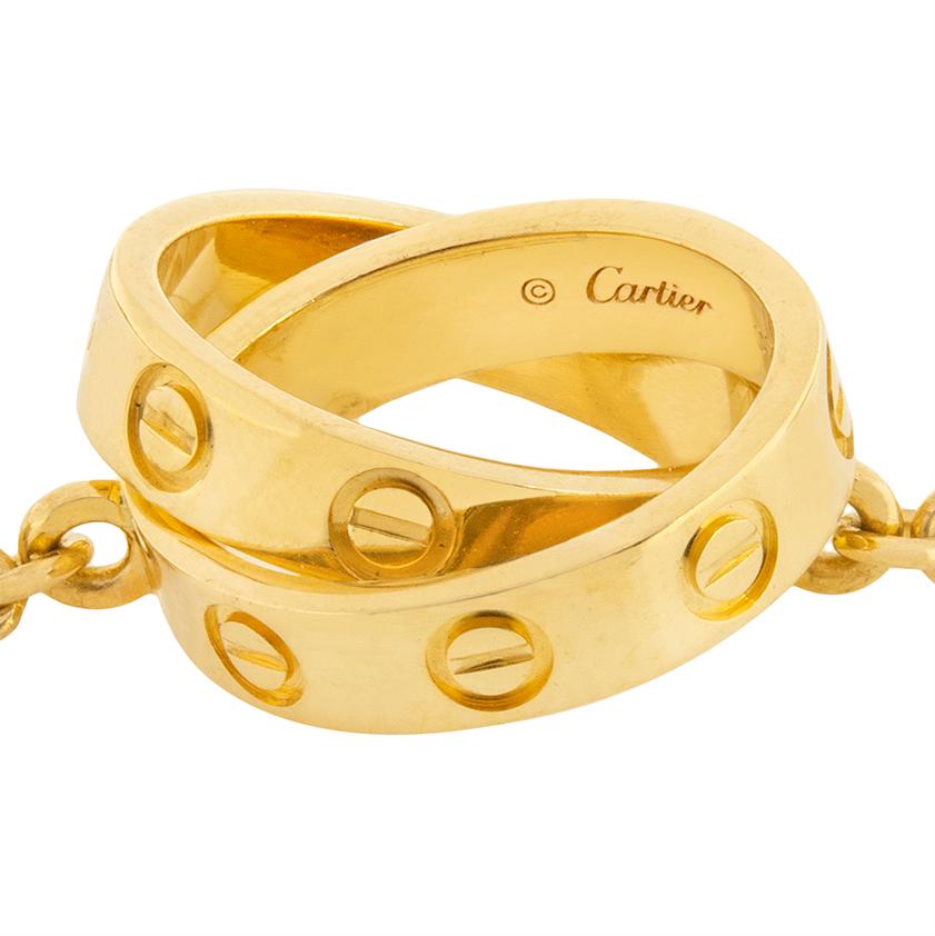 This sweet necklace is a part of the classic Cartier 'Love' collection. Two interlocking rings feature the screw motif characteristic of the 'Love' collection. The rings are on a chain with a claw closure. The entire necklace is made of 18 carat