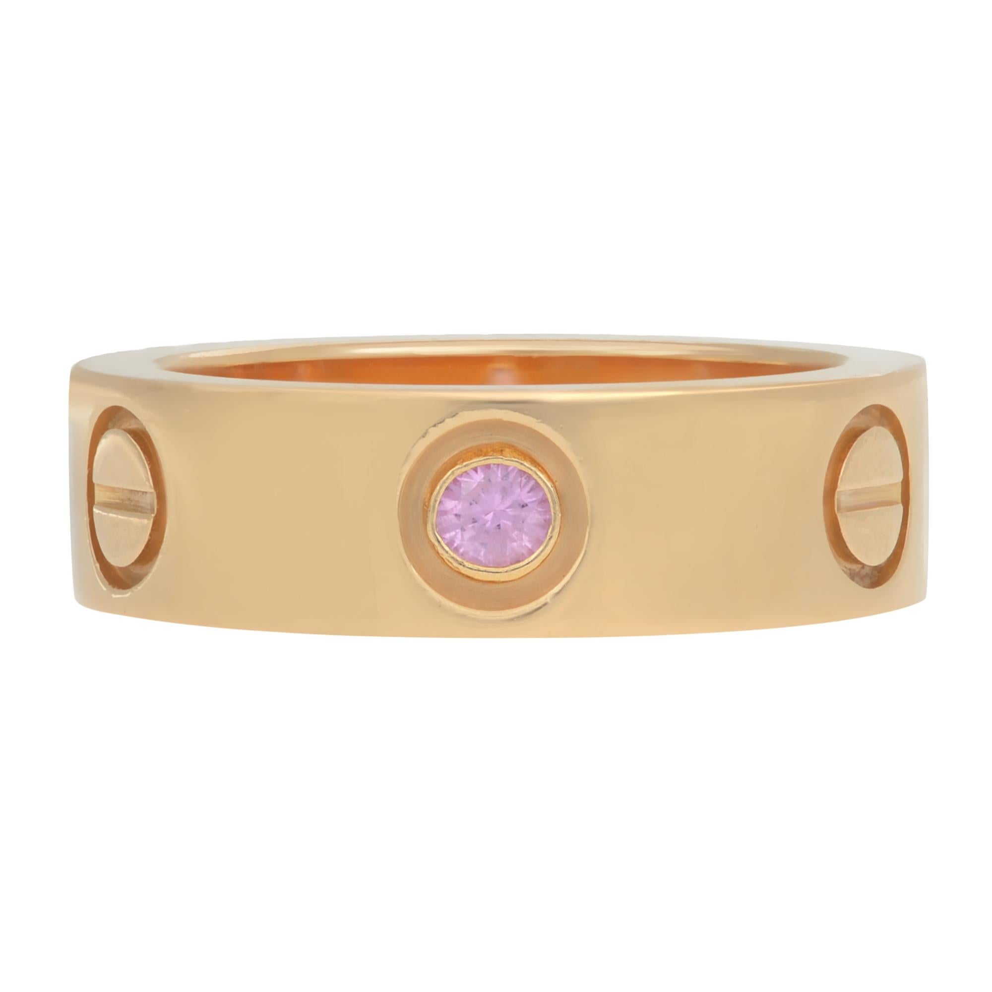 Cartier Love ring crafted in 1k rose gold and set with one round Pink Sapphire weighing an estimated 0.30 carats. Signed Cartier, 50, 750, with serial number. Ring size 50 US 5.25. Width: 5.60mm. Excellent pre-owned condition. Come with original box