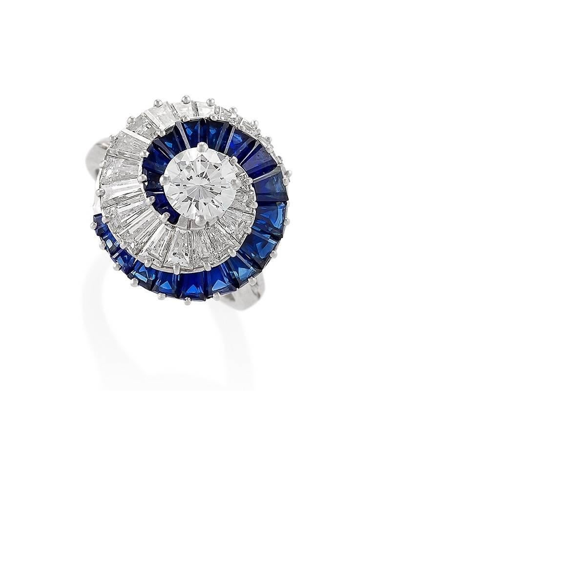A platinum ring with sapphires and diamonds by Cartier. The ring centers on a .90 carat round cut diamond, G/H color, VS clarity with 20 baguette-cut diamonds weighing a total of approximately 2.25 carats, G/H color, VS clarity. and 20 baguette