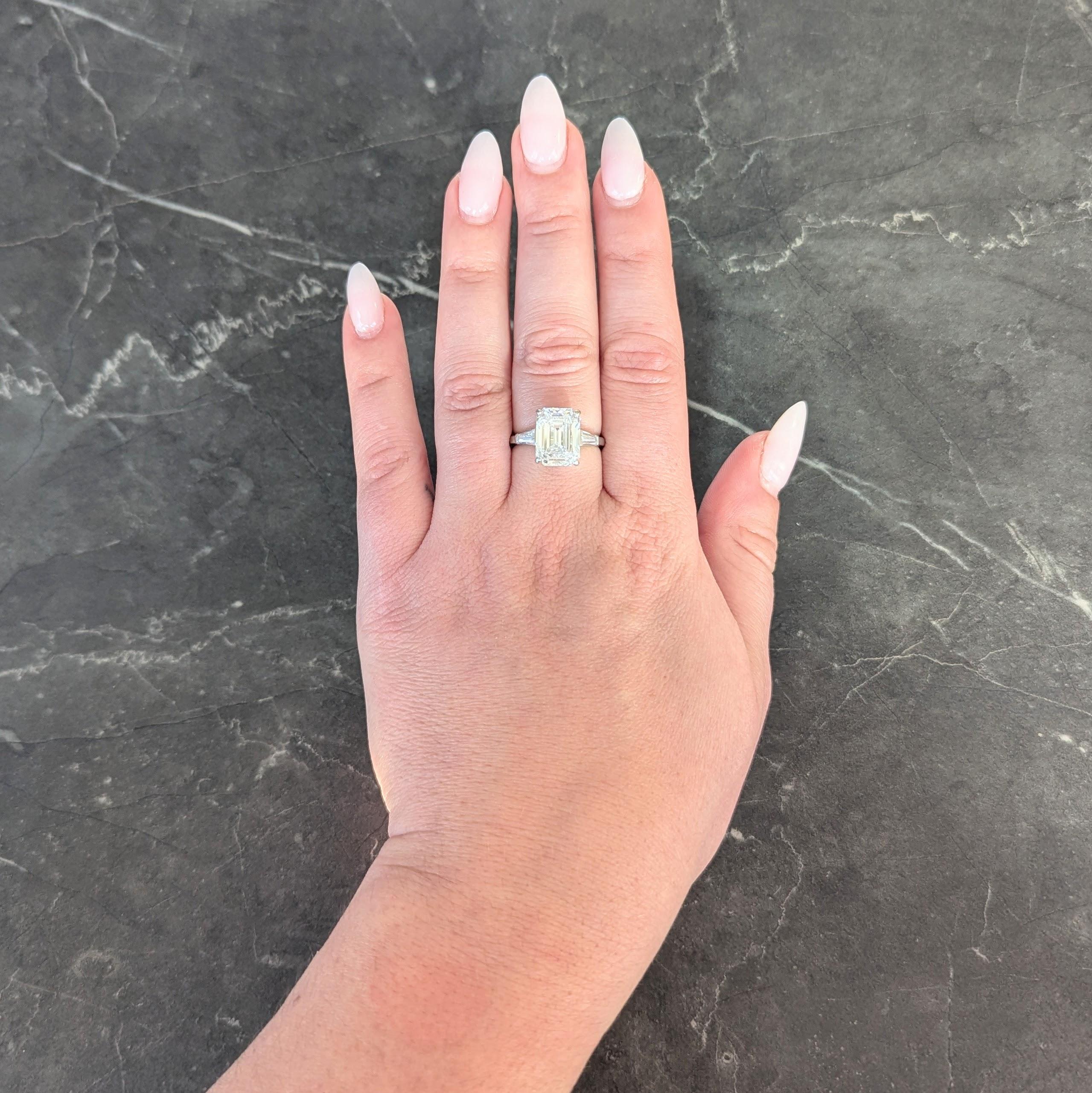 Engagement ring centers a prong set emerald cut diamond weighing 5.00 carats - D color with VS1 clarity
Flanked by two bar set and well matched tapered baguette cut diamonds 
Weighing approximately 0.40 carat total, D color with VS1