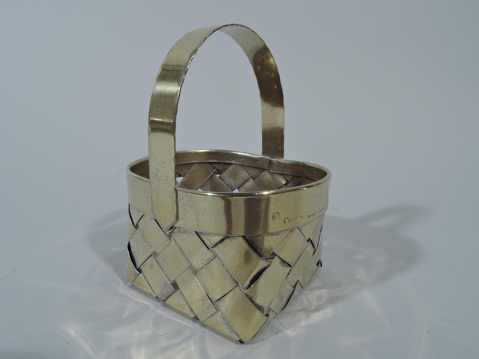 Mid-Century Modern sterling silver country chic basket. Retailed by Cartier in New York. Rectangular with curved ends. Plain rim and fixed C-scroll handle with “stitched” rims. Woven strips. The splurge-size version of the Classic high-low design