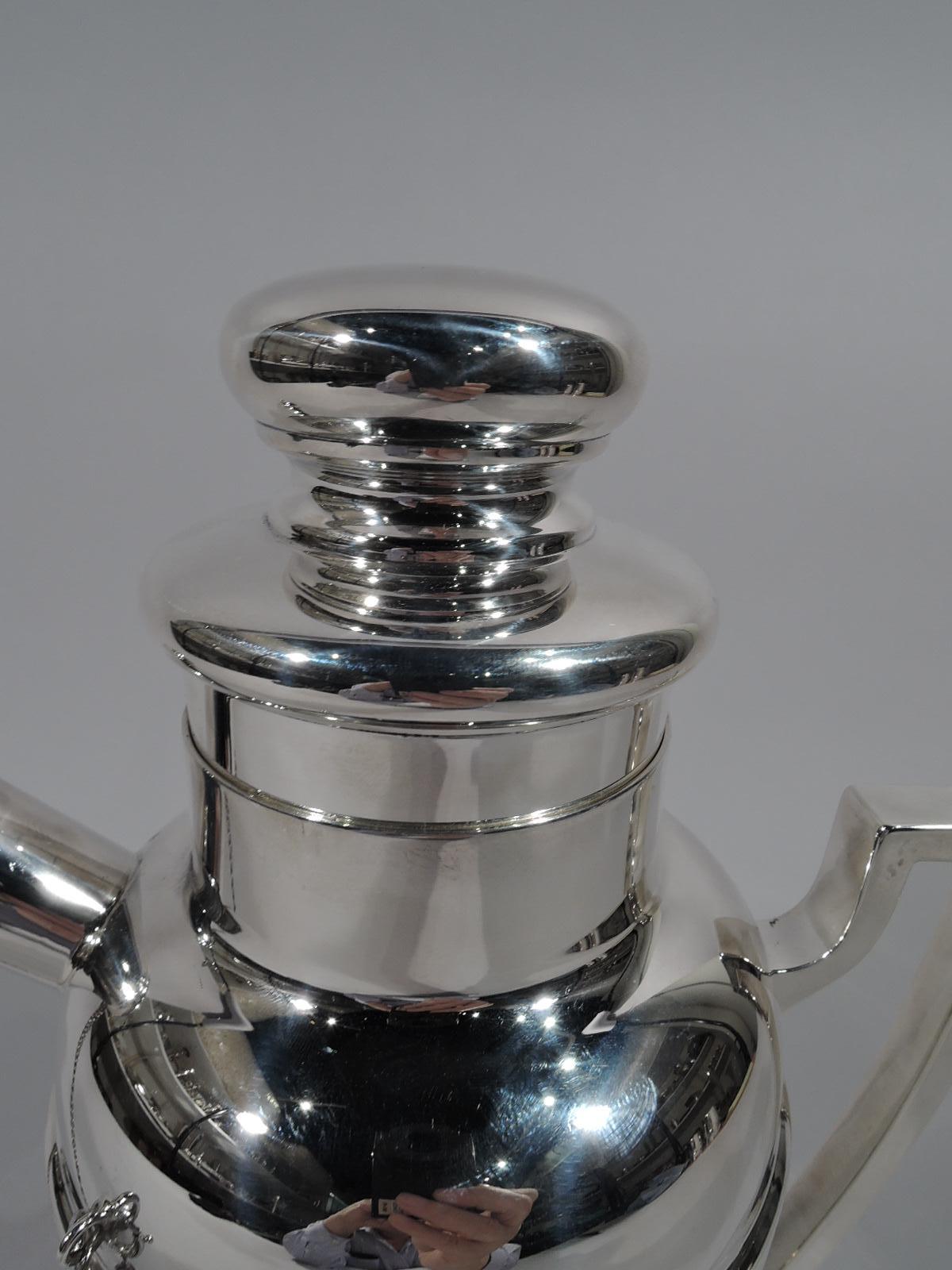Mid-Century Modern sterling silver cocktail Shaker. Retailed by Cartier in New York. Straight and tapering sides, curved shoulder, scroll bracket handle, and short inset neck. Stubby diagonal spout with built-in strainer and chained cap. Cover
