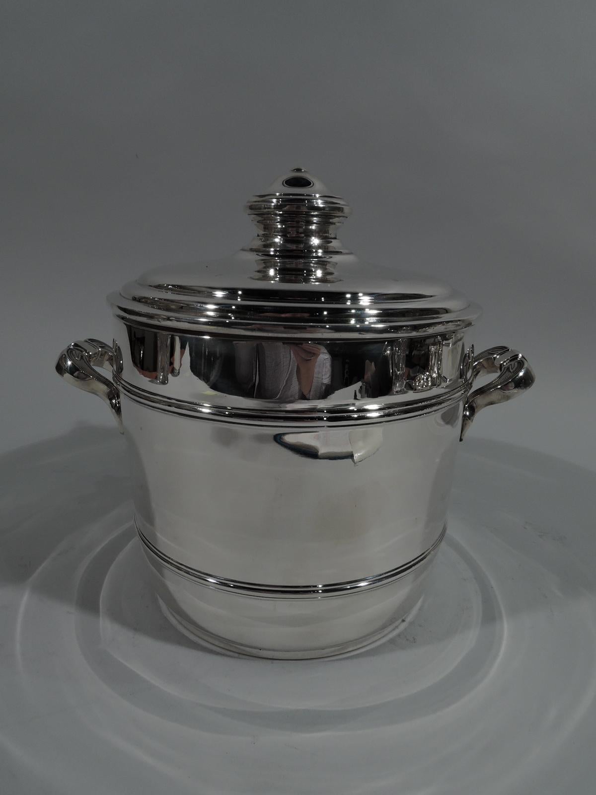 Mid-Century Modern sterling silver ice bucket with tongs. Retailed by Cartier in New York. Gently curved barrel body with two molded staves, double-scrolled side handles, and leaf-capped scrolled hook. Cover stepped with large and stepped finial.
