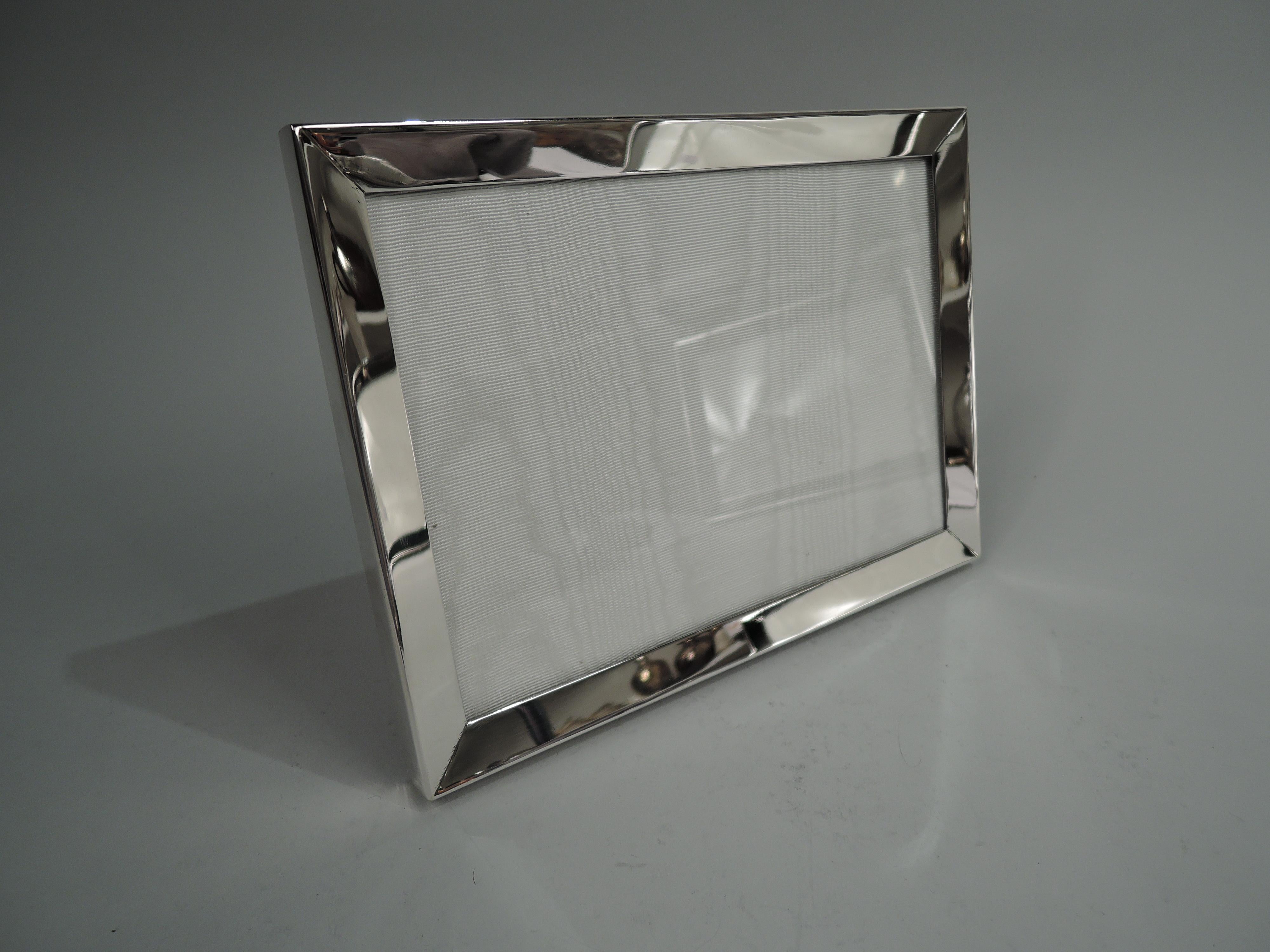 Modern sterling silver picture frame. Retailed by Cartier in New York. Rectangular window in same surround with tapering front and flat sides. Midcentury chic in hard-to-find landscape form. With glass, silk lining, and laminate back and hinged
