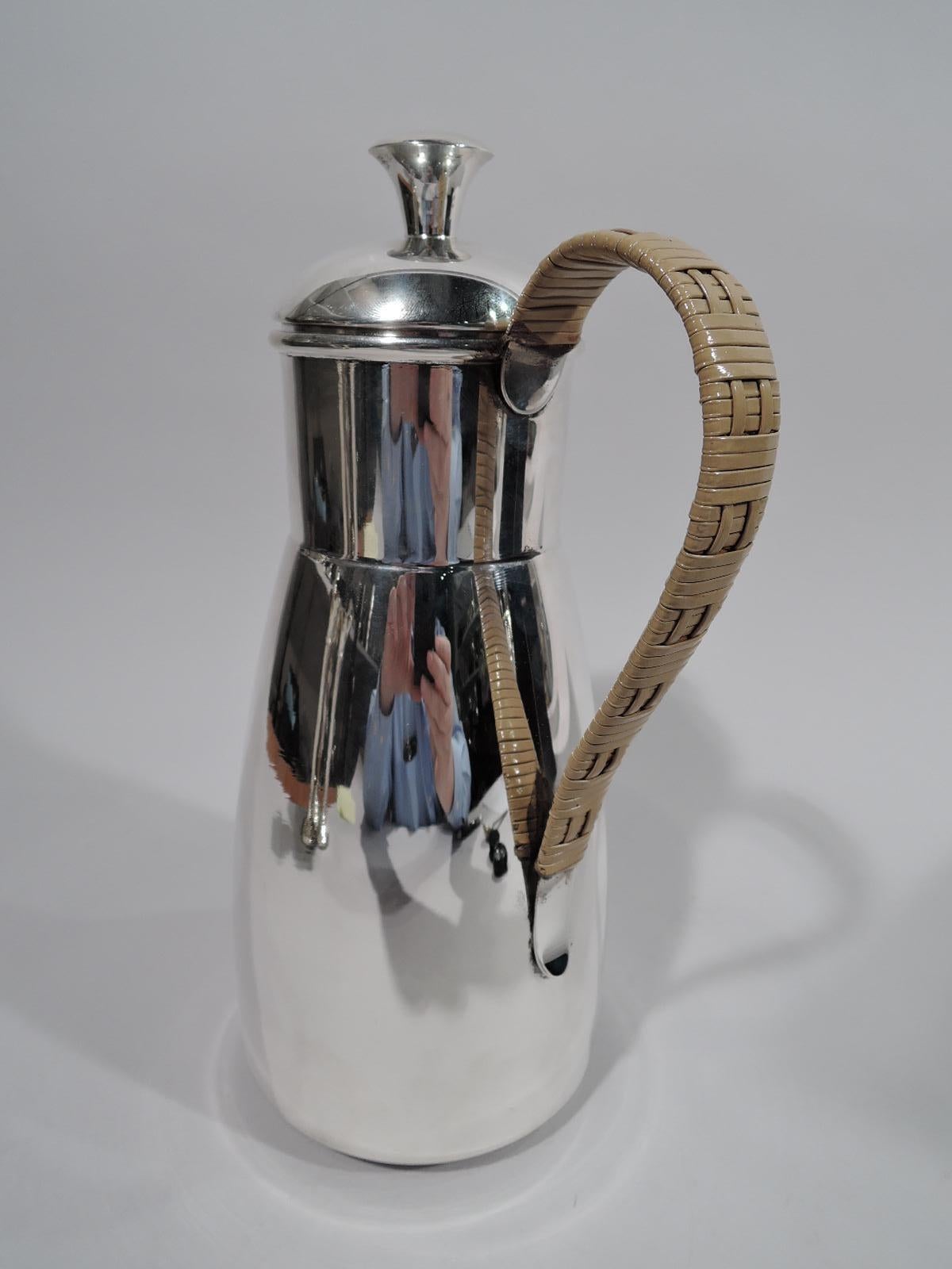 Mid-Century Modern sterling silver martini pitcher. Retailed by Cartier in New York. Truncated cone body, straight drum-form neck, v-spout with built in strainer, and domed cover. Handle scrolled and wrapped in rattan-style weave. Fully marked