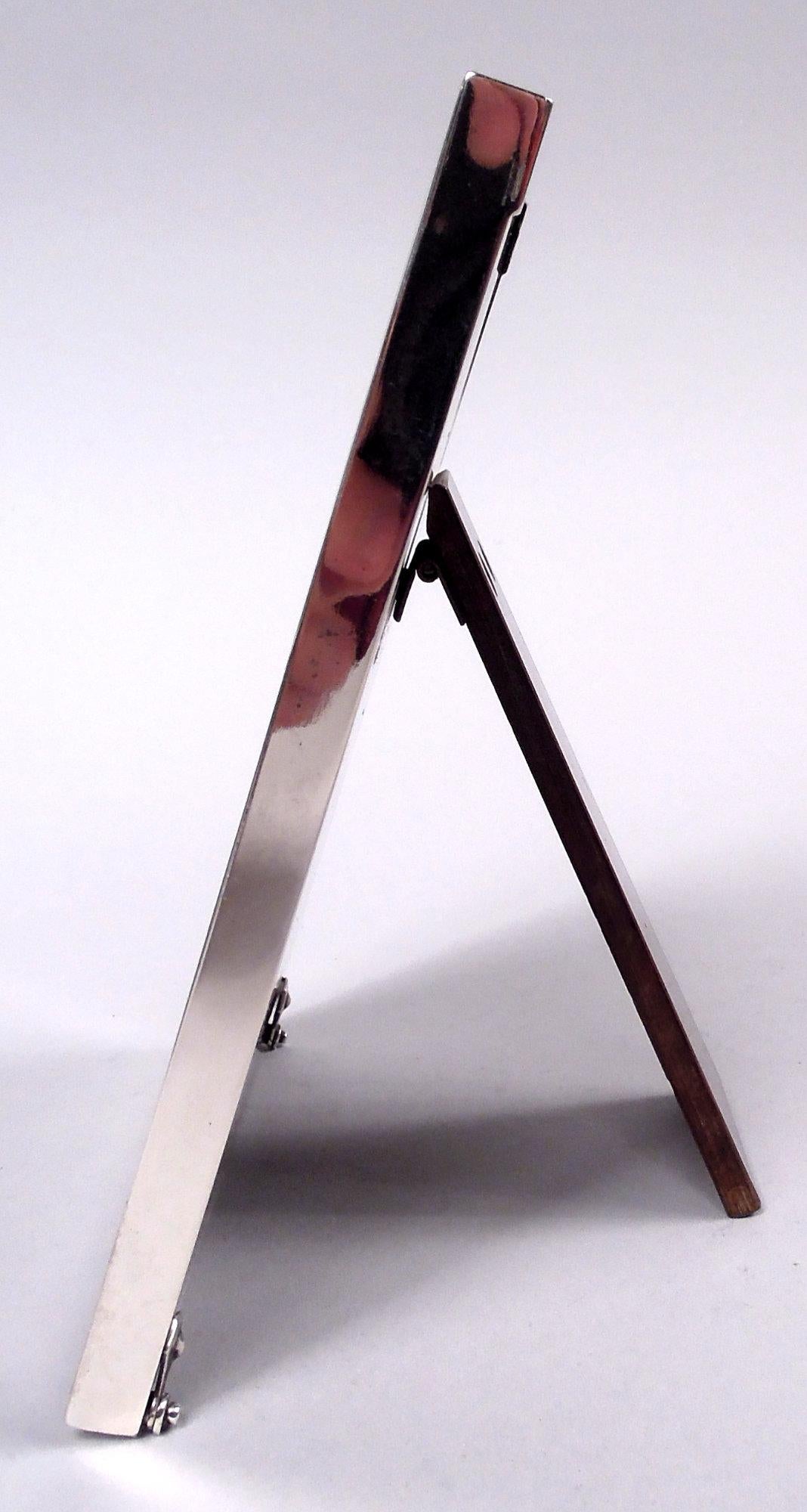 American Midcentury Modern sterling silver picture frame. Retailed by Cartier in New York. Flat and plain rectangular surround. With glass, silk lining, and wood laminate back and hinged easel support for portrait (vertical) display. Marks include