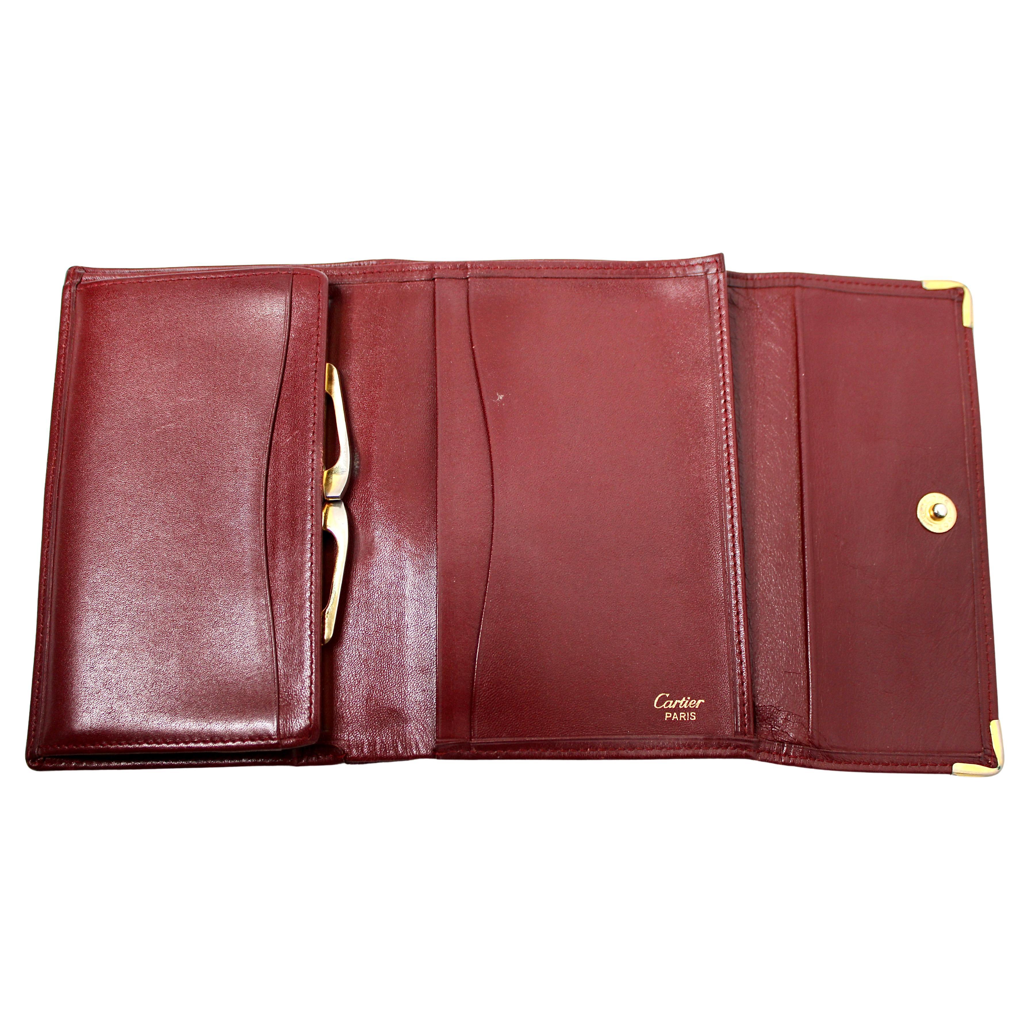 Il portafoglio trifold in pelle bordeaux Must de Cartier, risalente agli anni '80, è un pezzo senza tempo che emana raffinatezza e lusso classici. Realizzato in pelle bordeaux di alta qualità, questo portafoglio presenta l'iconico logo Cartier