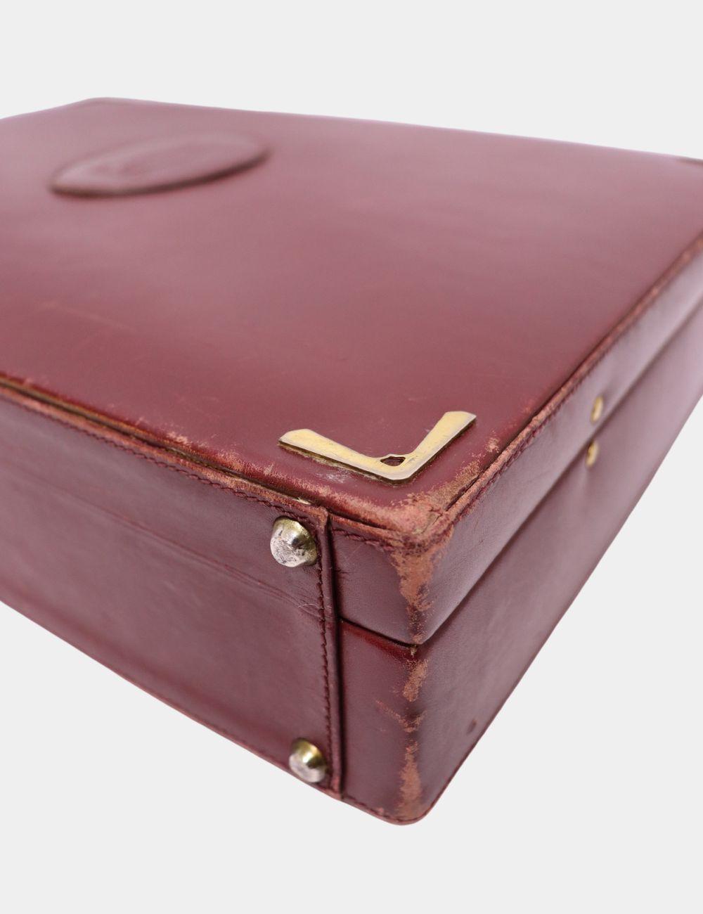 Refined and iconic, this Cartier Burgundy Leather Briefcase from the Must de Cartier collection is the epitome of timeless sophistication. Crafted in luxurious deep burgundy leather with gold-tone corner hardware, this structured business case