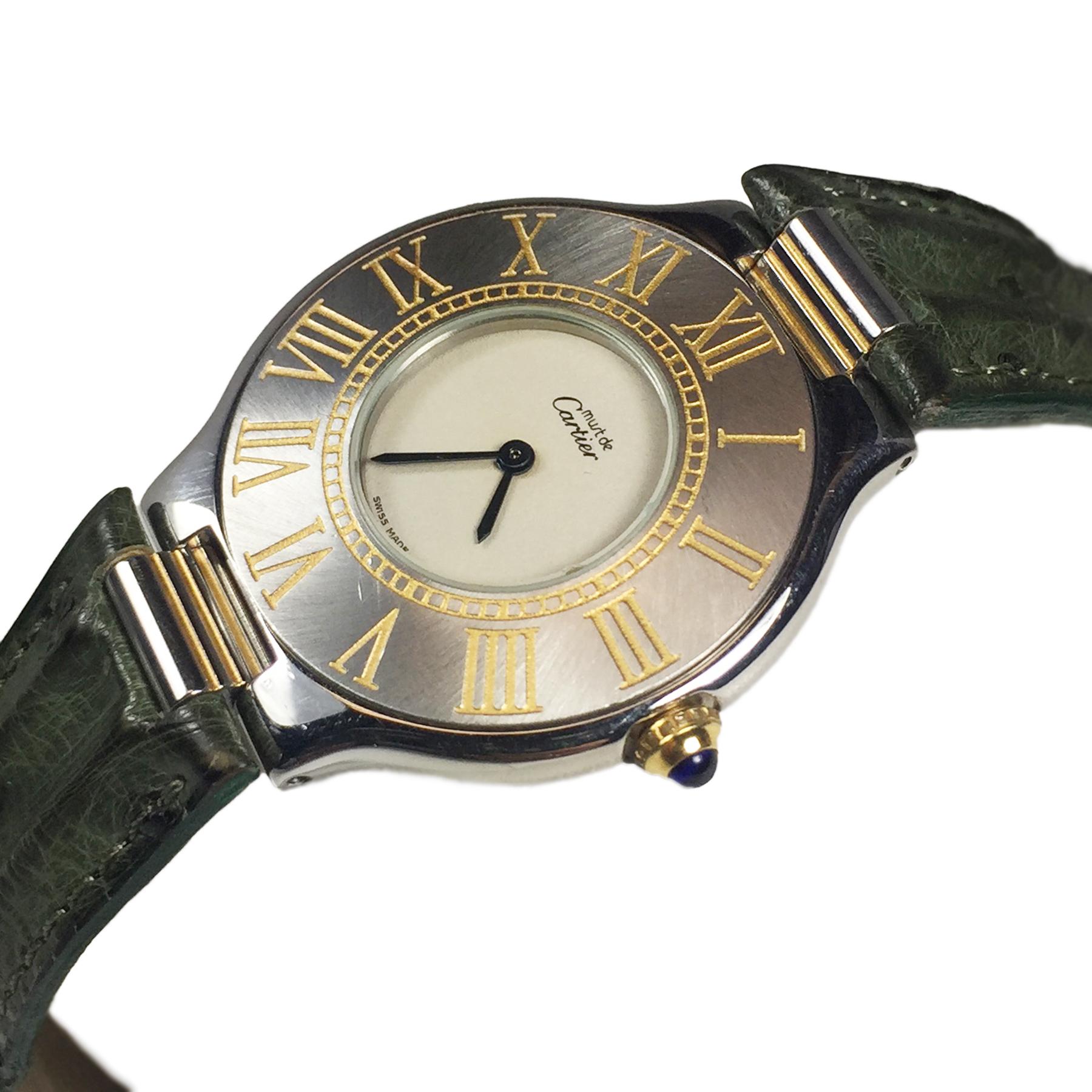 Circa 1990s Cartier, Must De cartier 21 Wrist watch, 31 MM Stainless Steel with Gold accents case and a Gold crown set with a
Sapphire. Quartz Movement, White Dial,  5/8 inch wide original Cartier padded Green strap with Cartier Deployment clasp.