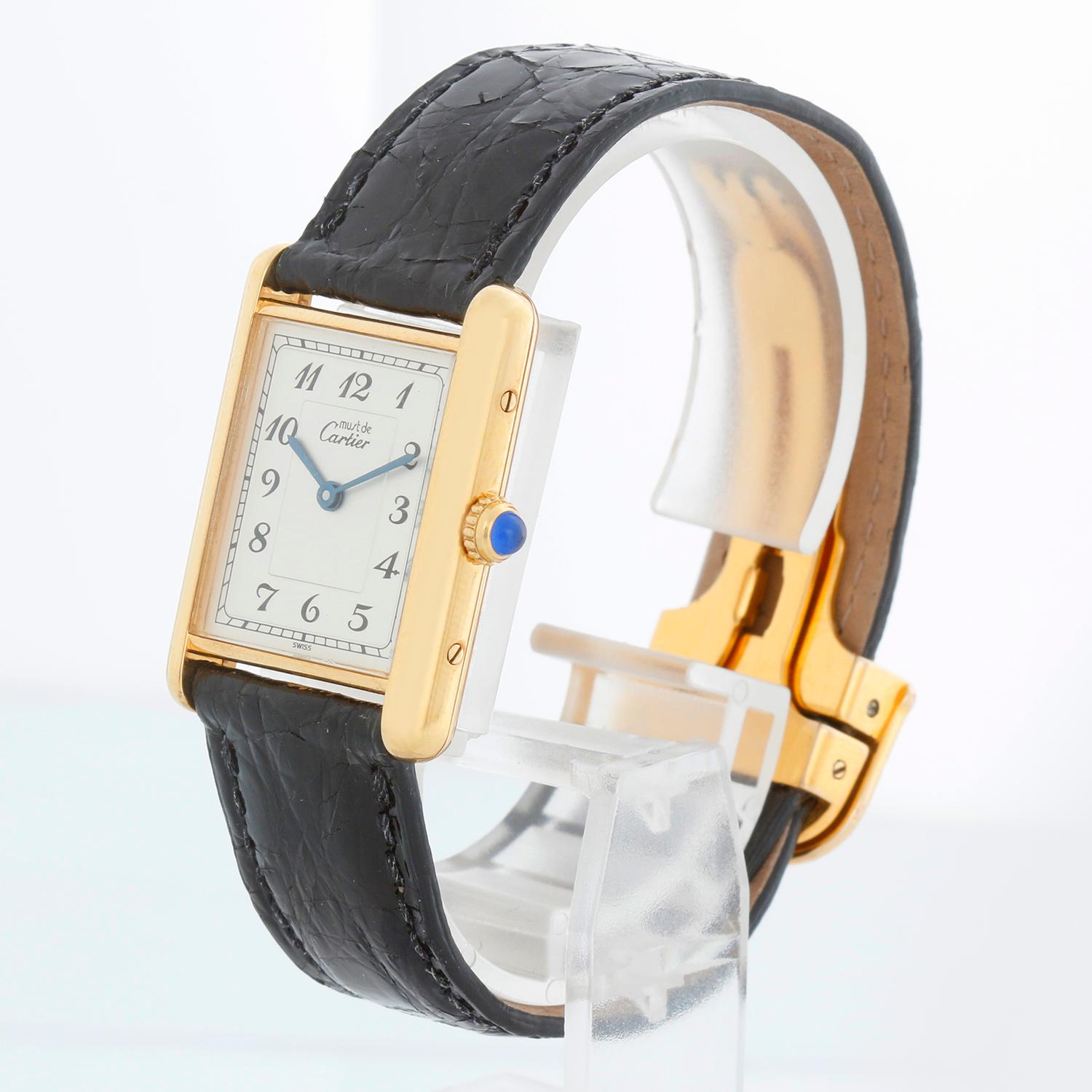 Reloj Cartier Must de Tank Placa de Oro 1615 para señora - Movimiento de cuarzo. Tanque Must de Cartier. Caja con placa de oro ( 22 mm x 30 mm ). Esfera plateada con números Breguet. Correa Cartier negra con cierre desplegable Cartier. Seminuevo con